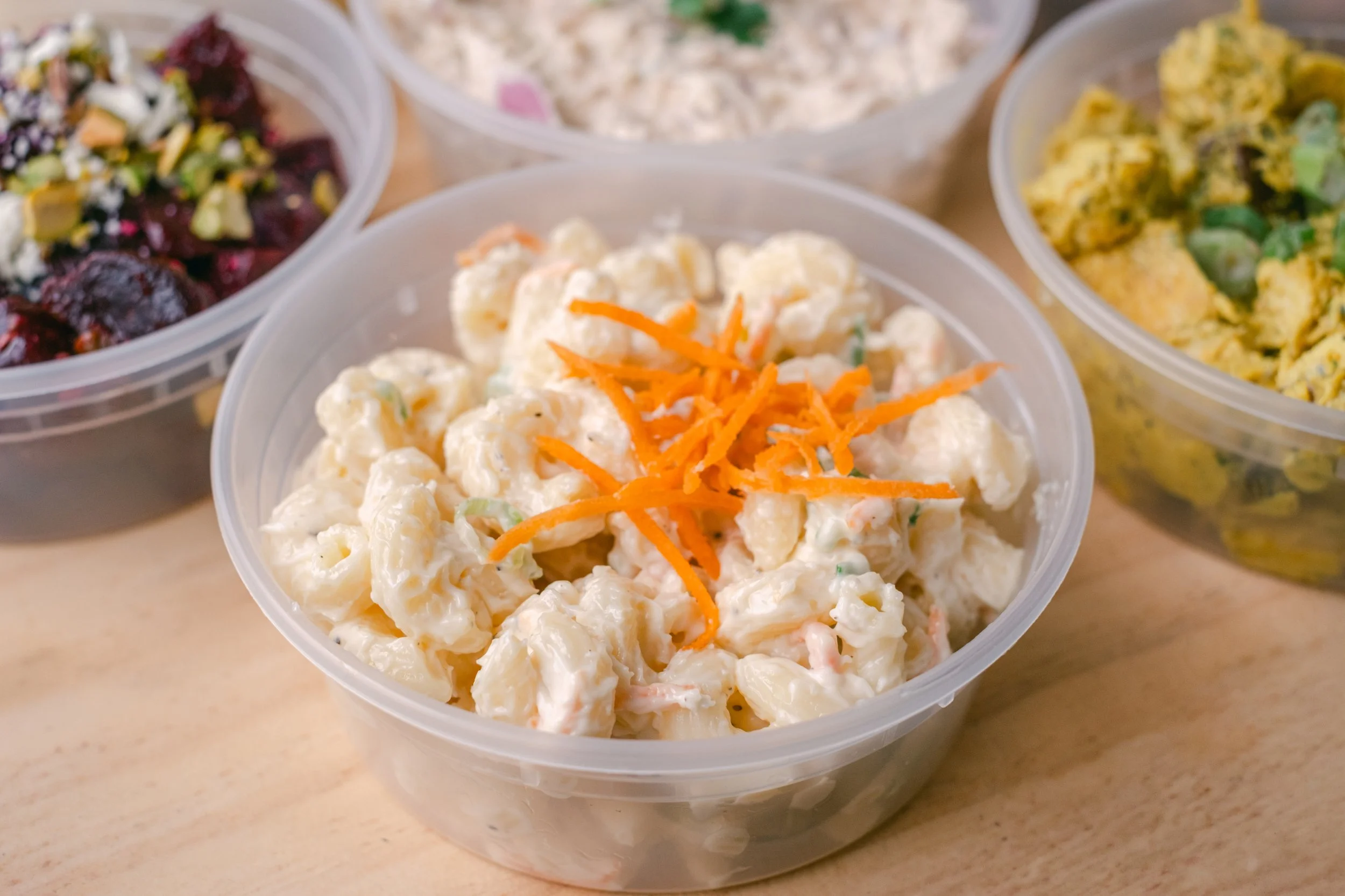 Containers of potato salad with shredded carrots, a vegetable salad, and creamy salads.