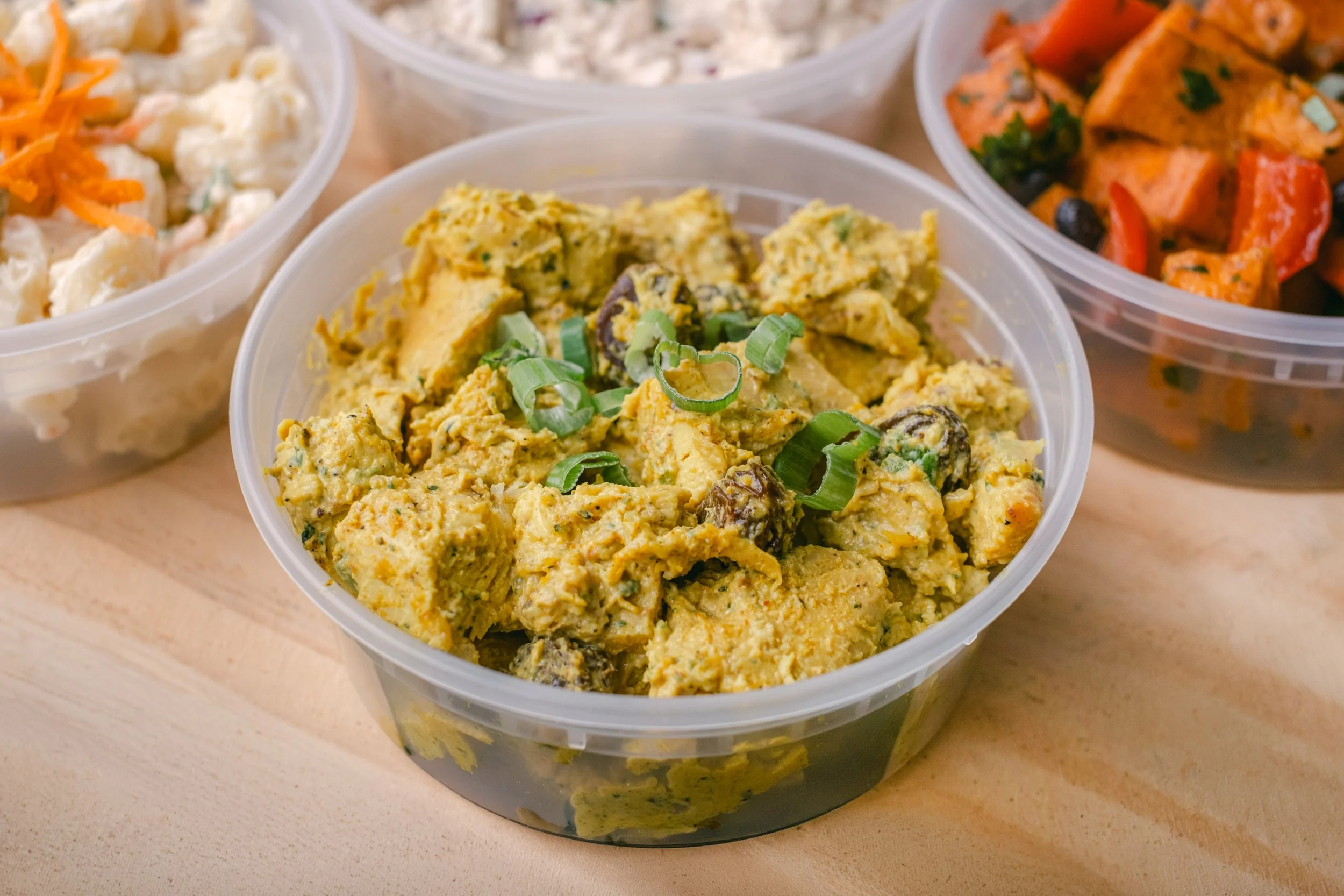 Close-up of a food container filled with a creamy chicken salad garnished with chopped green onions.