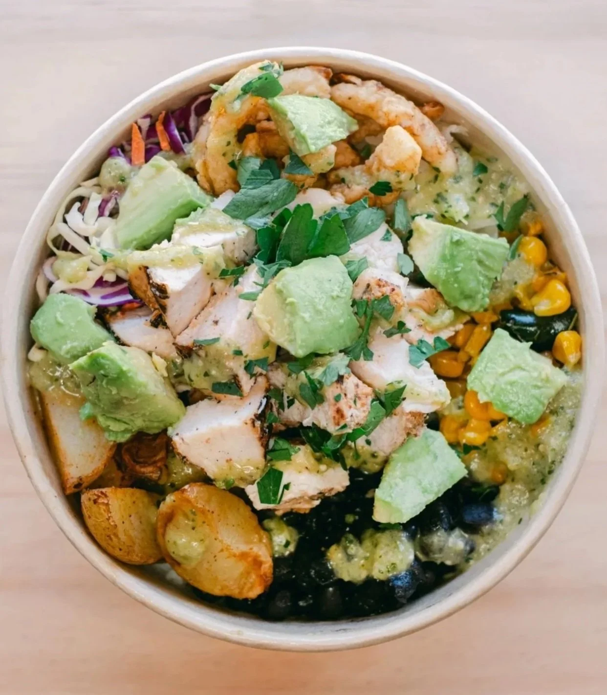 A bowl of burrito bowl with grilled chicken, avocado, black beans, corn, shredded cabbage, and fresh cilantro.
