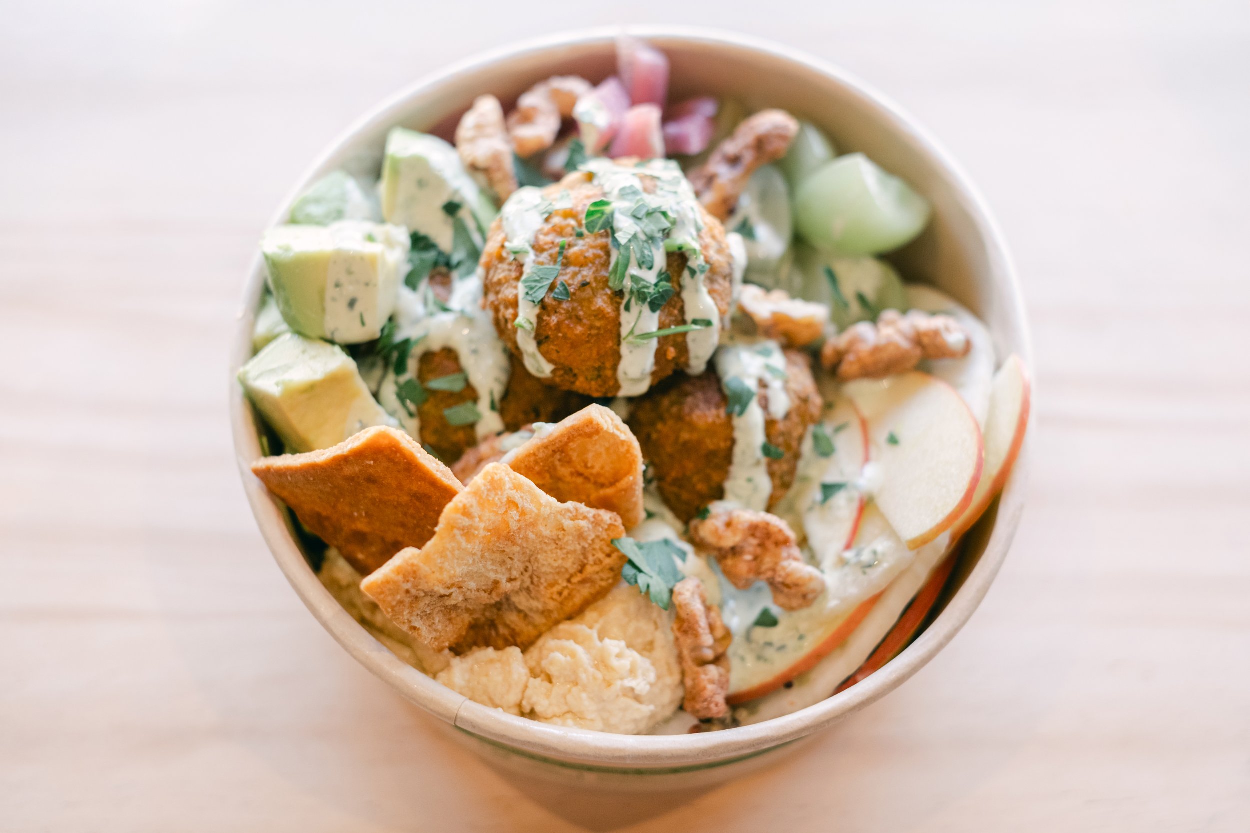 A bowl of chopped avocado, fried chicken pieces topped with herbs, and various chips, served with a creamy dressing or sauce.