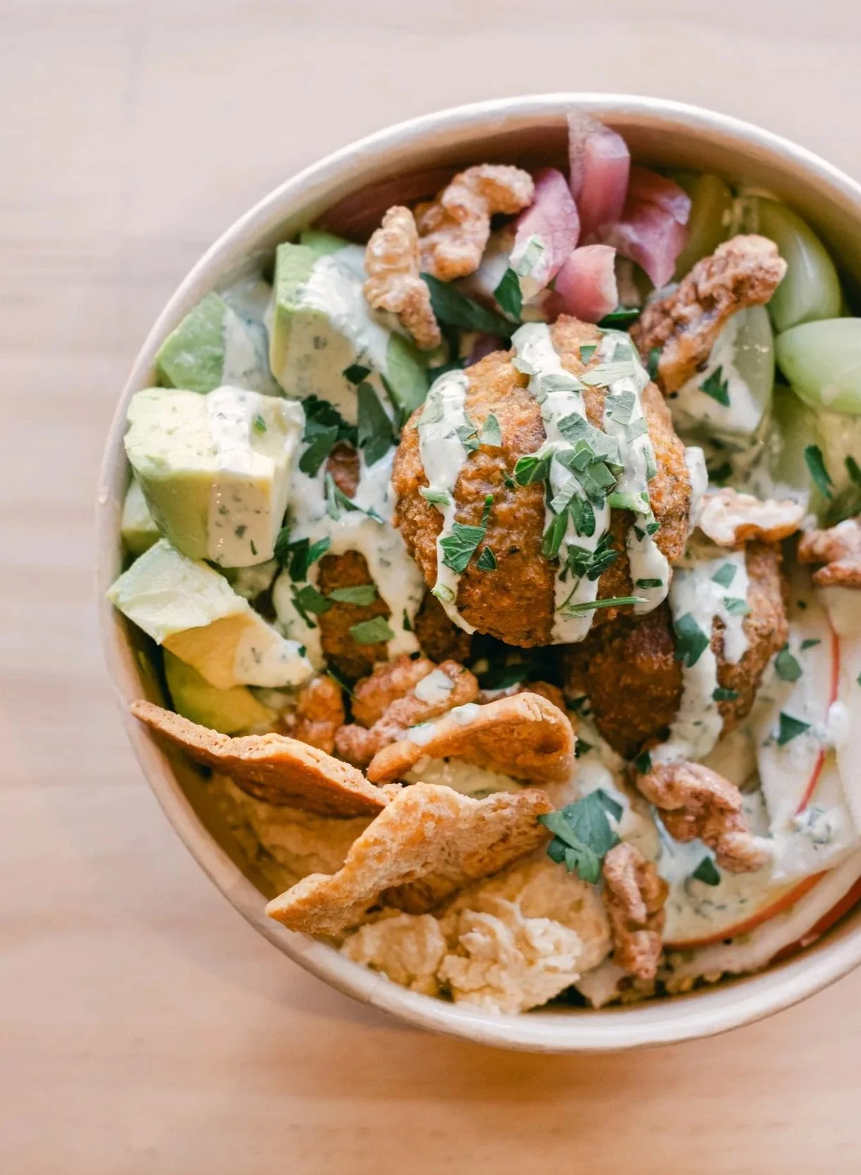 Bowl of fried chicken, avocado, crackers, and salad with herbs and dressing.