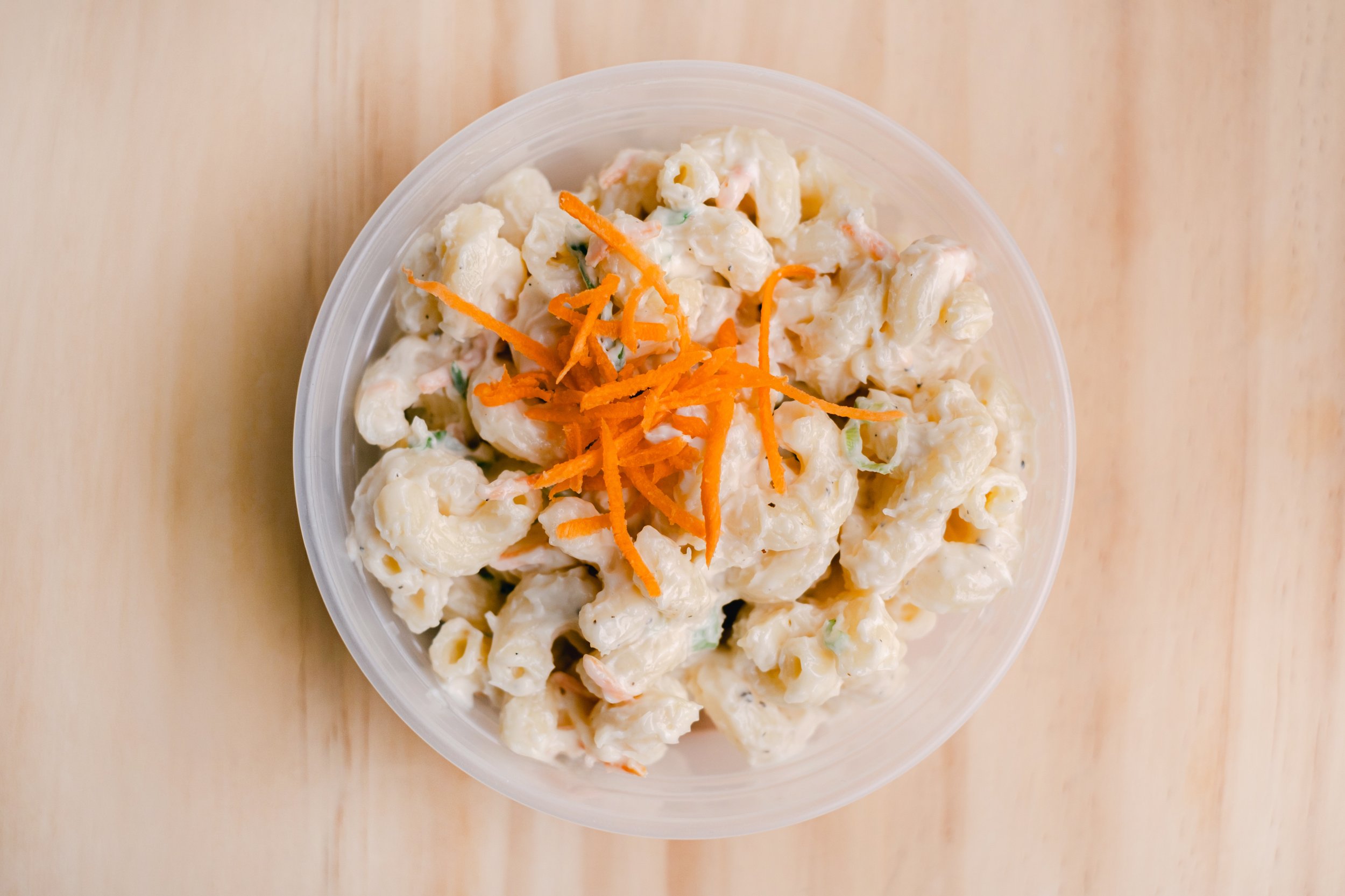 A bowl of potato salad topped with shredded carrots on a wooden surface.