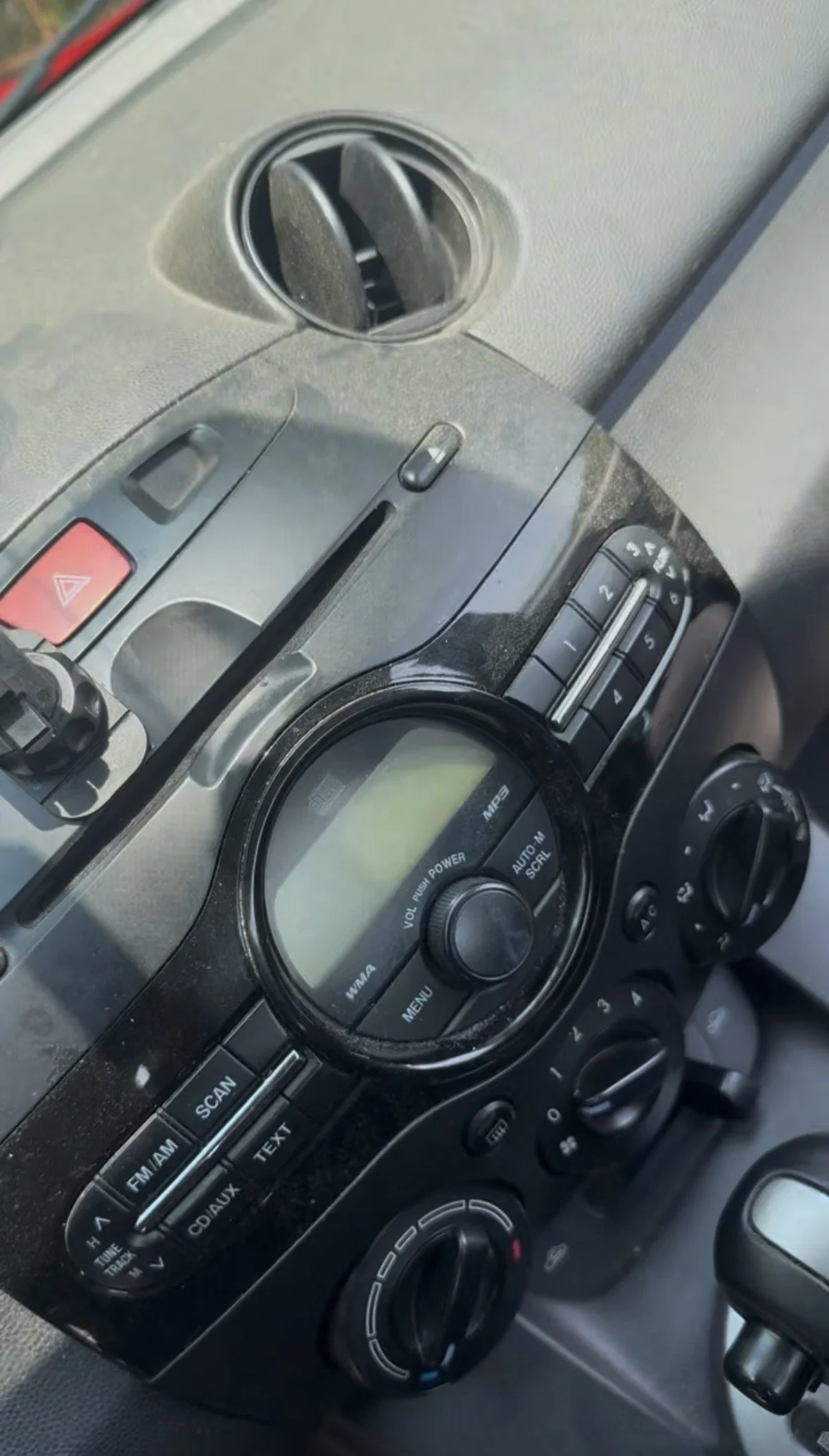 Close-up of a car dashboard with an air vent, radio controls, and climate control dials.