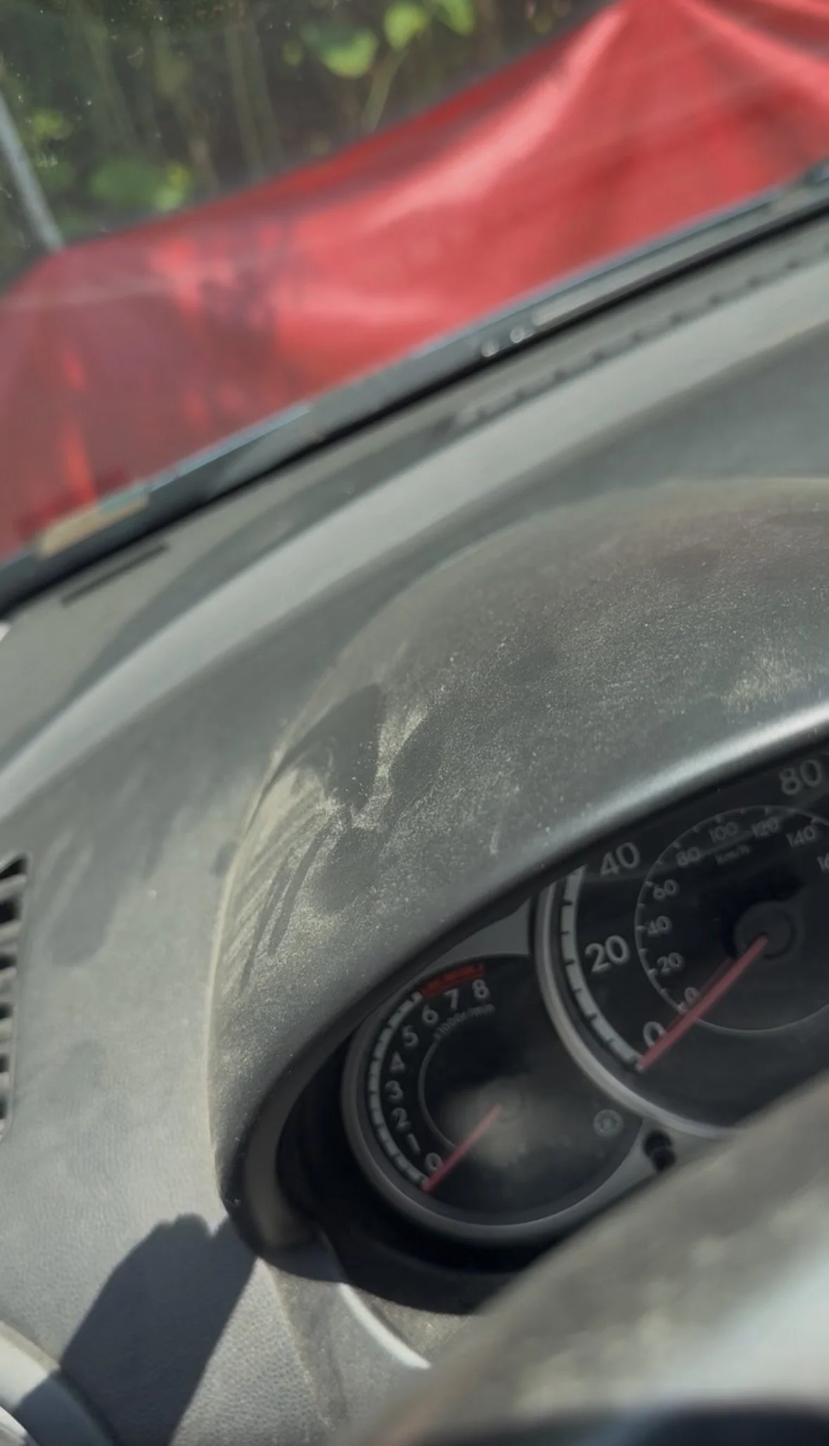 Close-up of a car dashboard showing the speedometer and tachometer with a red object just outside the windshield.