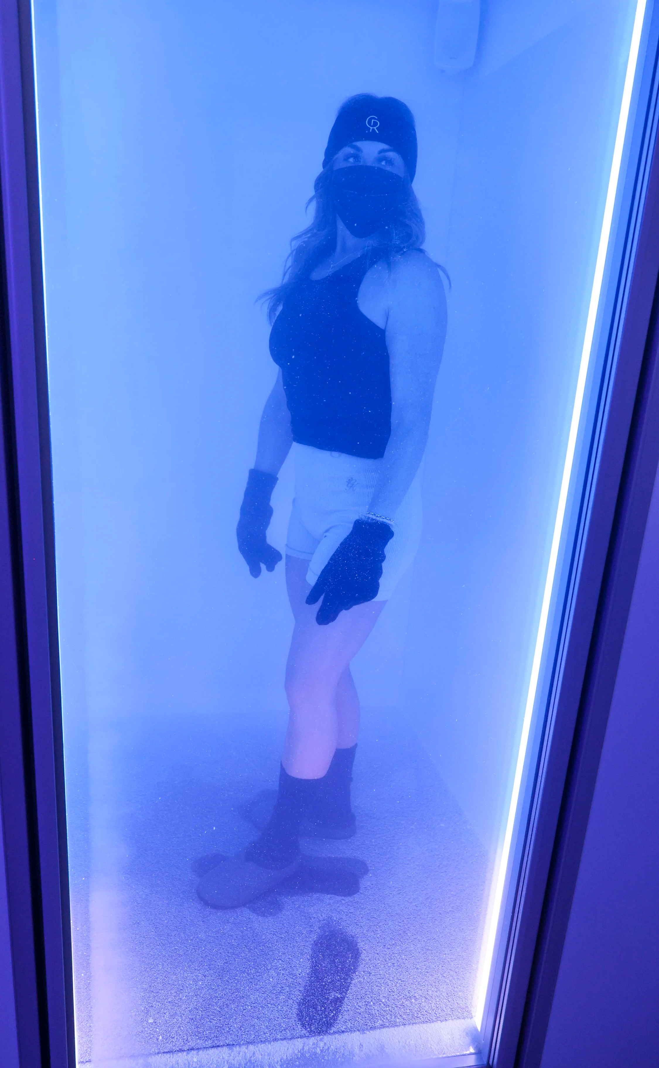 A client wearing a protective face mask stands inside The Cold Room's -87°C full body cryotherapy chamber.
