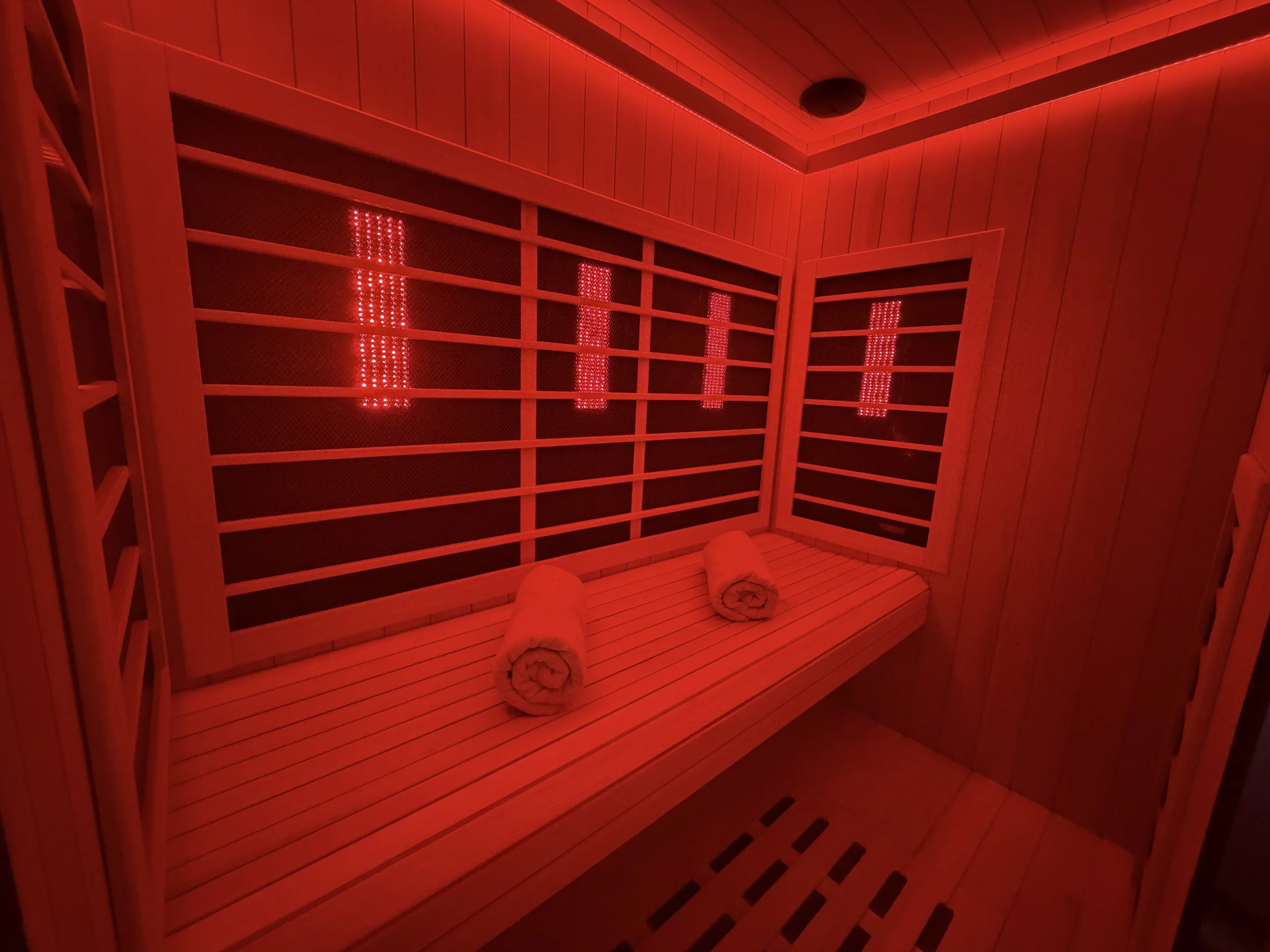 The Cold Room's Sunlighten infrared sauna room with wooden benches, privacy doors, and rolled towels placed on the bench.