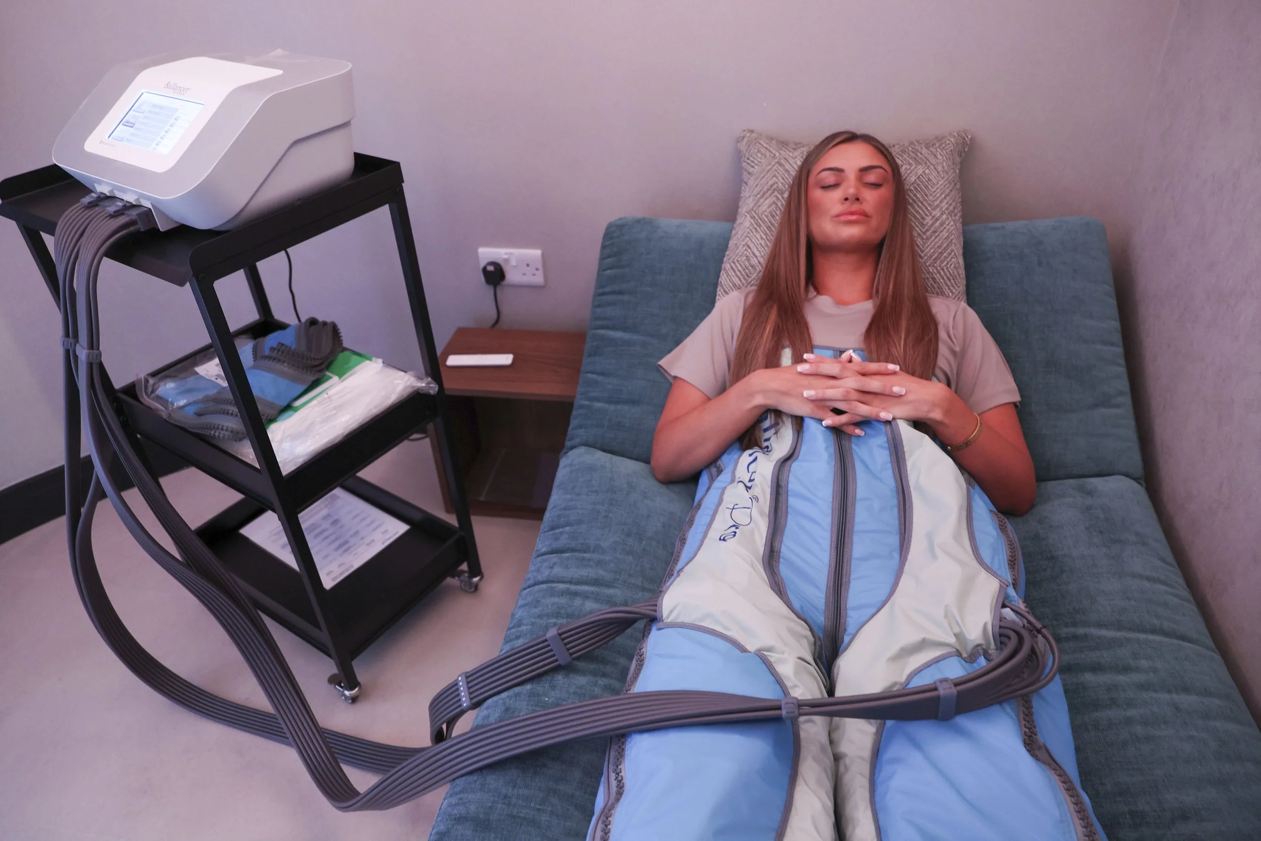A client is relaxing and enjoying the benefits of The Cold Room's Body Ballancer. You can see the control unit and lower body compression suit in the private treatment room.