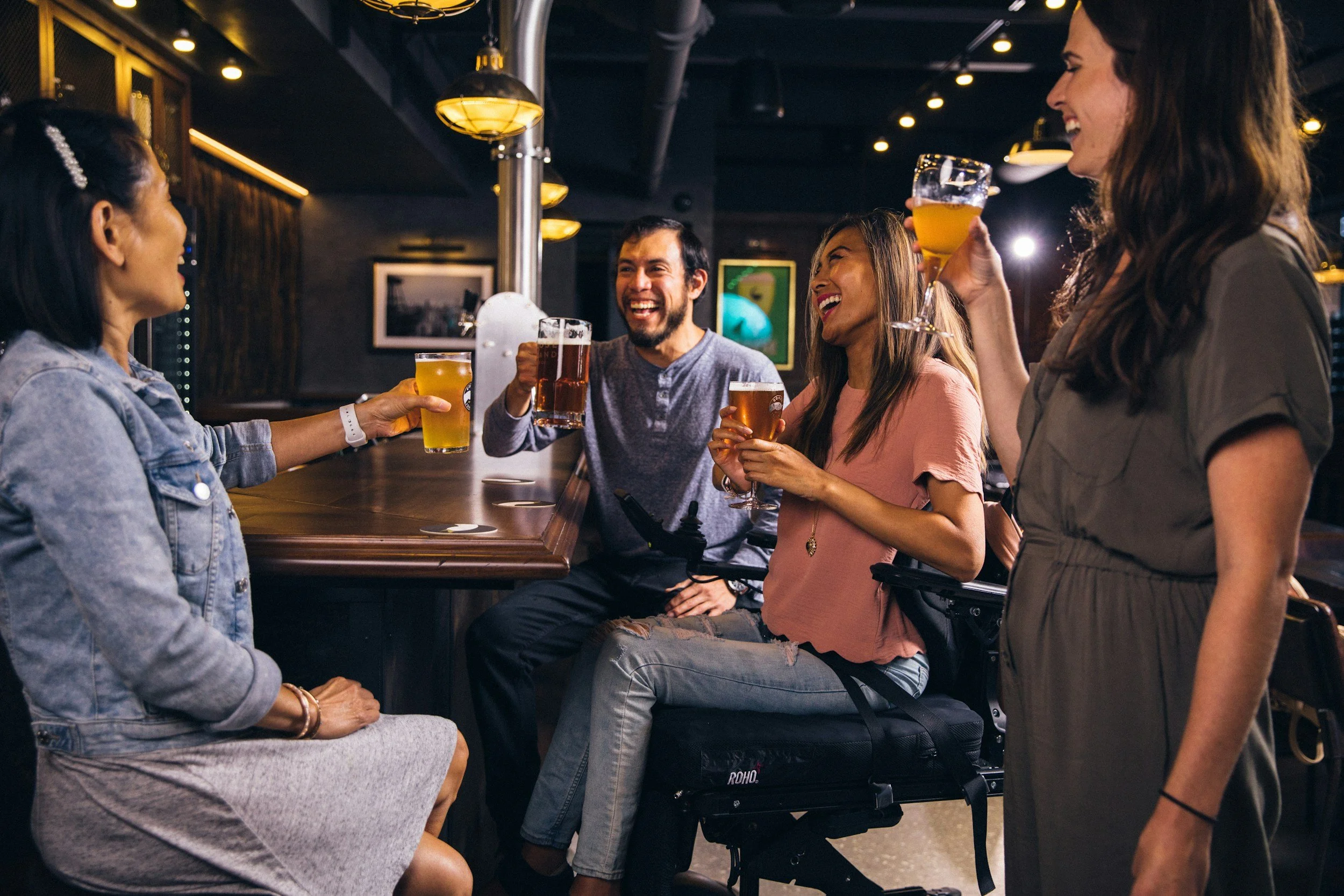Fünf Menschen, vier Frauen und ein Mann, lachen und trinken Bier in einer Bar.