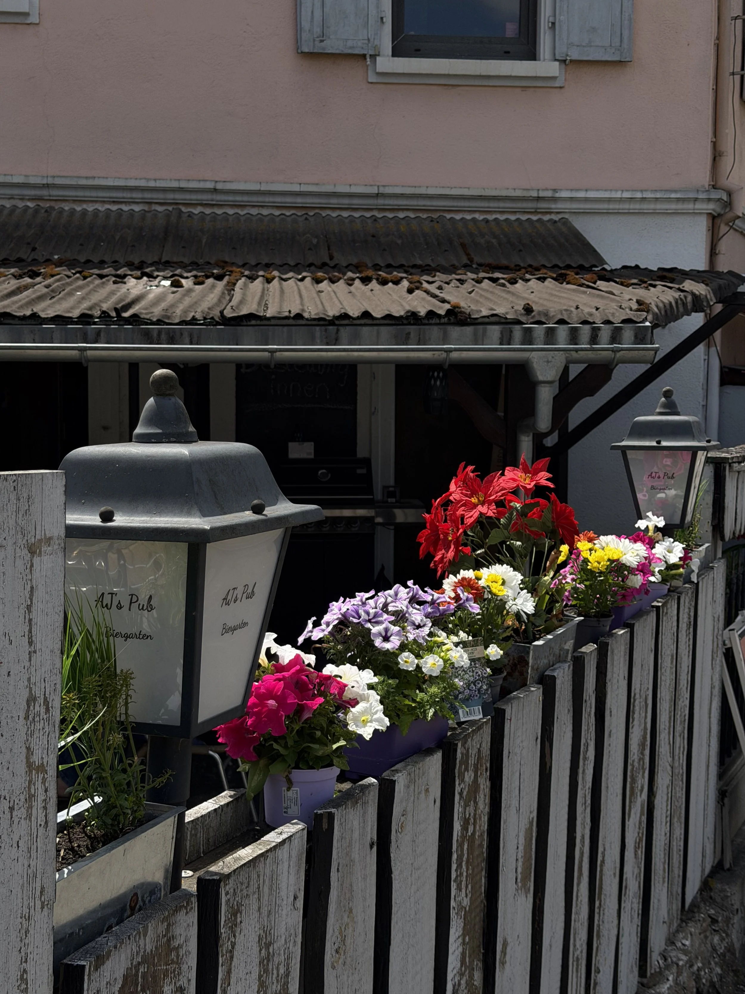 Blumenständer mit bunten Blumen vor einem weißen Holzzaun.