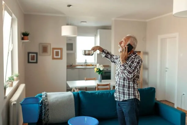 An elderly man speaking on the phone while holding a frying pan in a living room.