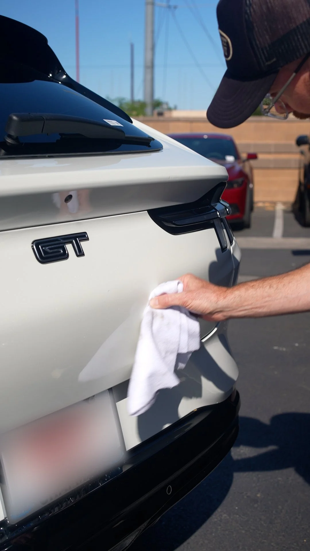 Person cleaning the rear of a white car with a cloth, focusing on the GT badge on the trunk, the finishing process of a paint touch-up