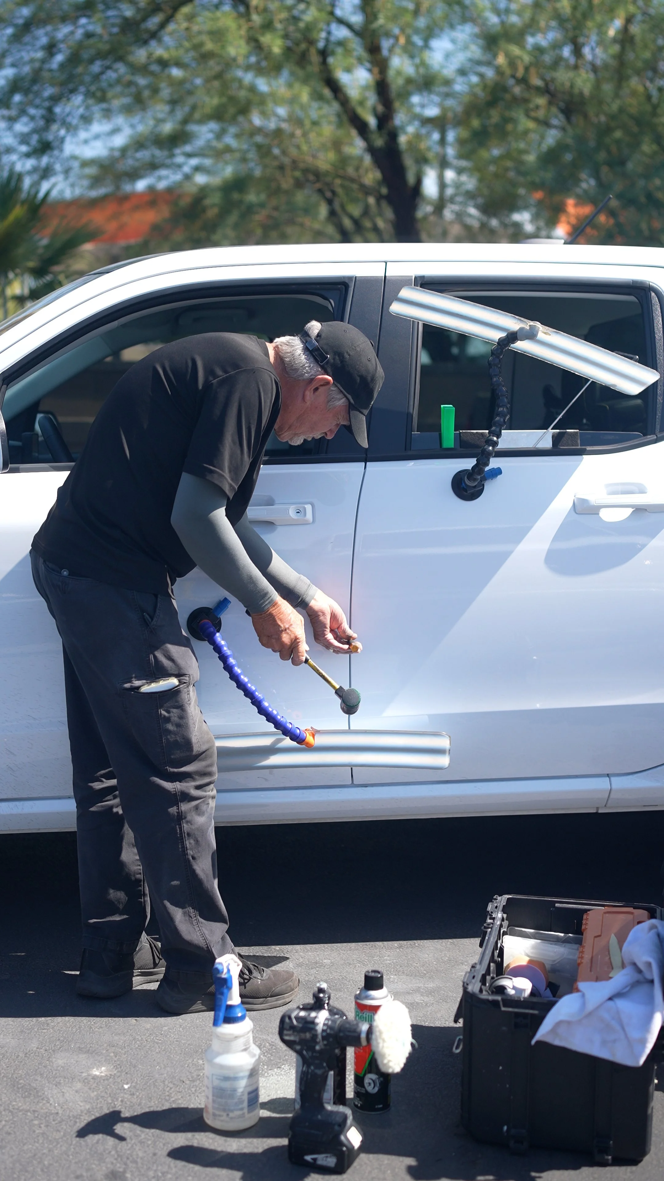 A white car being fixed with Paintless Dent repair, in a dealer lot. This car will look like it never had dents in it once DRS applies their PDR service.