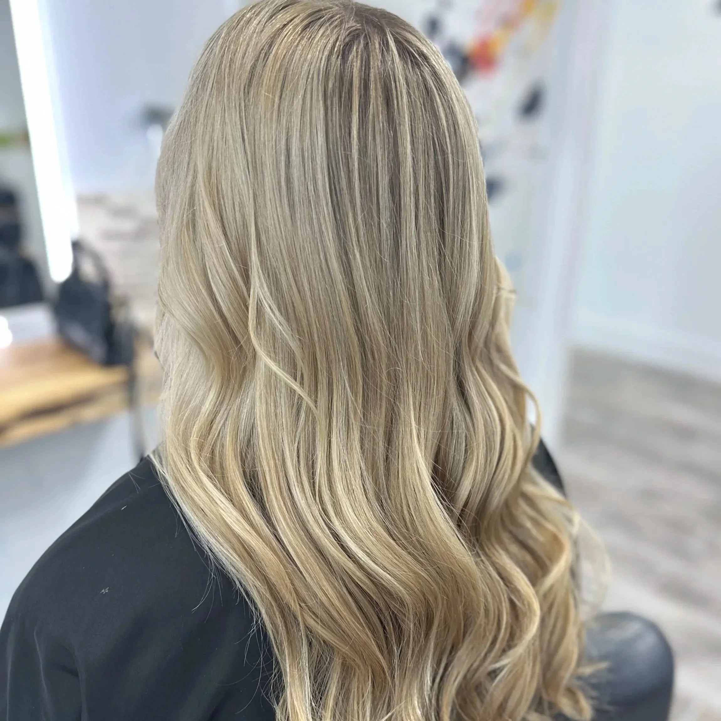 Close-up of long, straight blonde hair from the back of a person, with a blurred background.