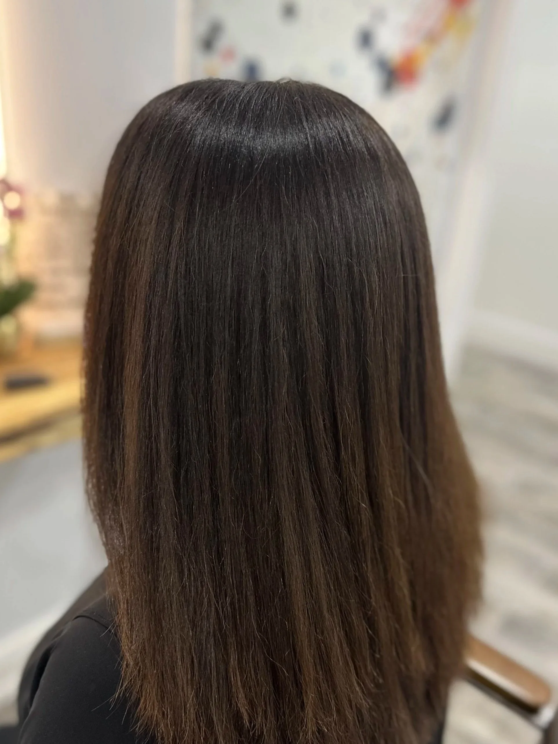 Close-up of a person's long, straight, shiny brown hair seen from the back.