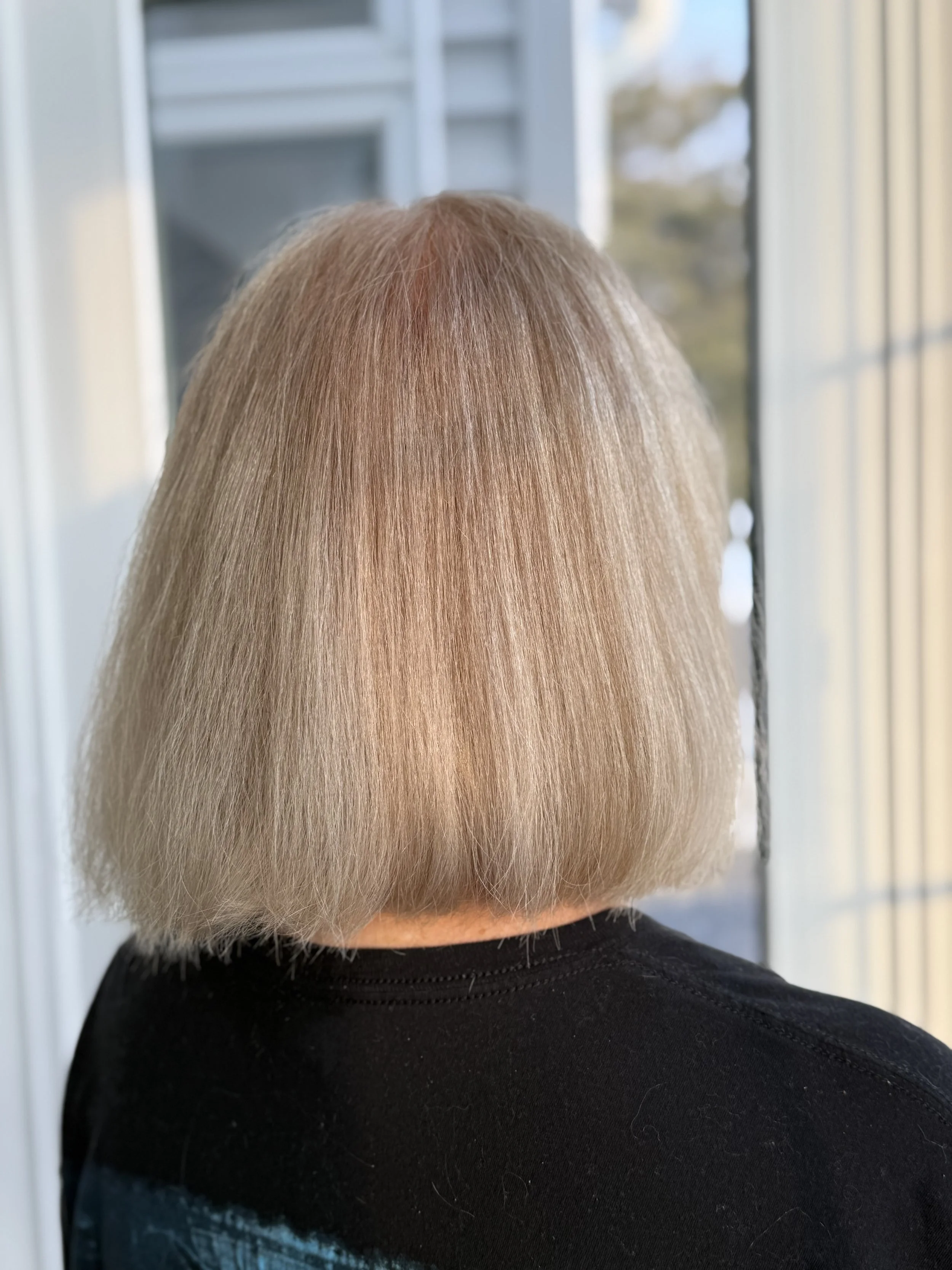 Back view of a person with short blonde hair standing in front of a window.