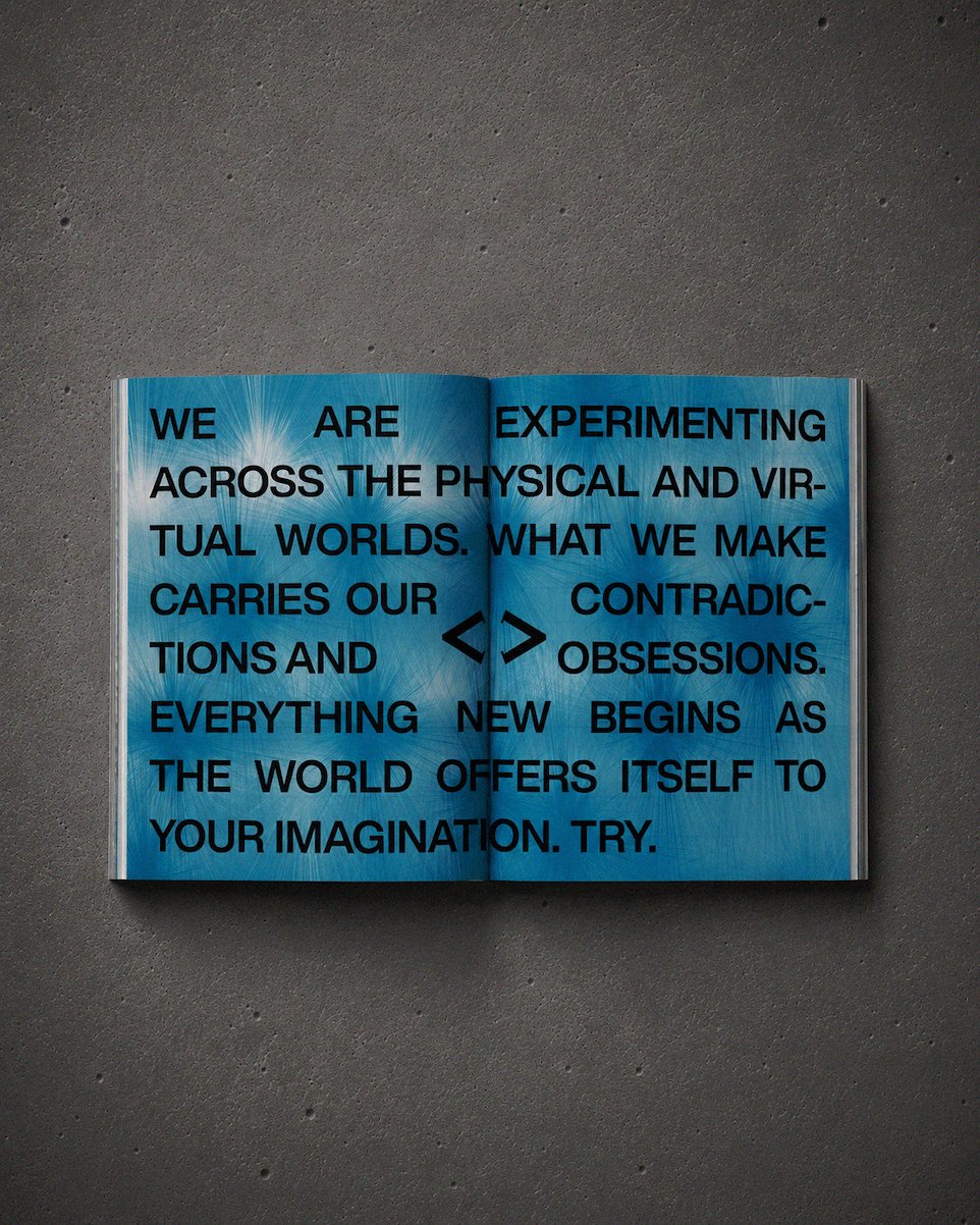 Open book with blue background and black text on a gray textured surface. The text discusses exploring physical and virtual worlds, contradictions, obsessions, and new beginnings.