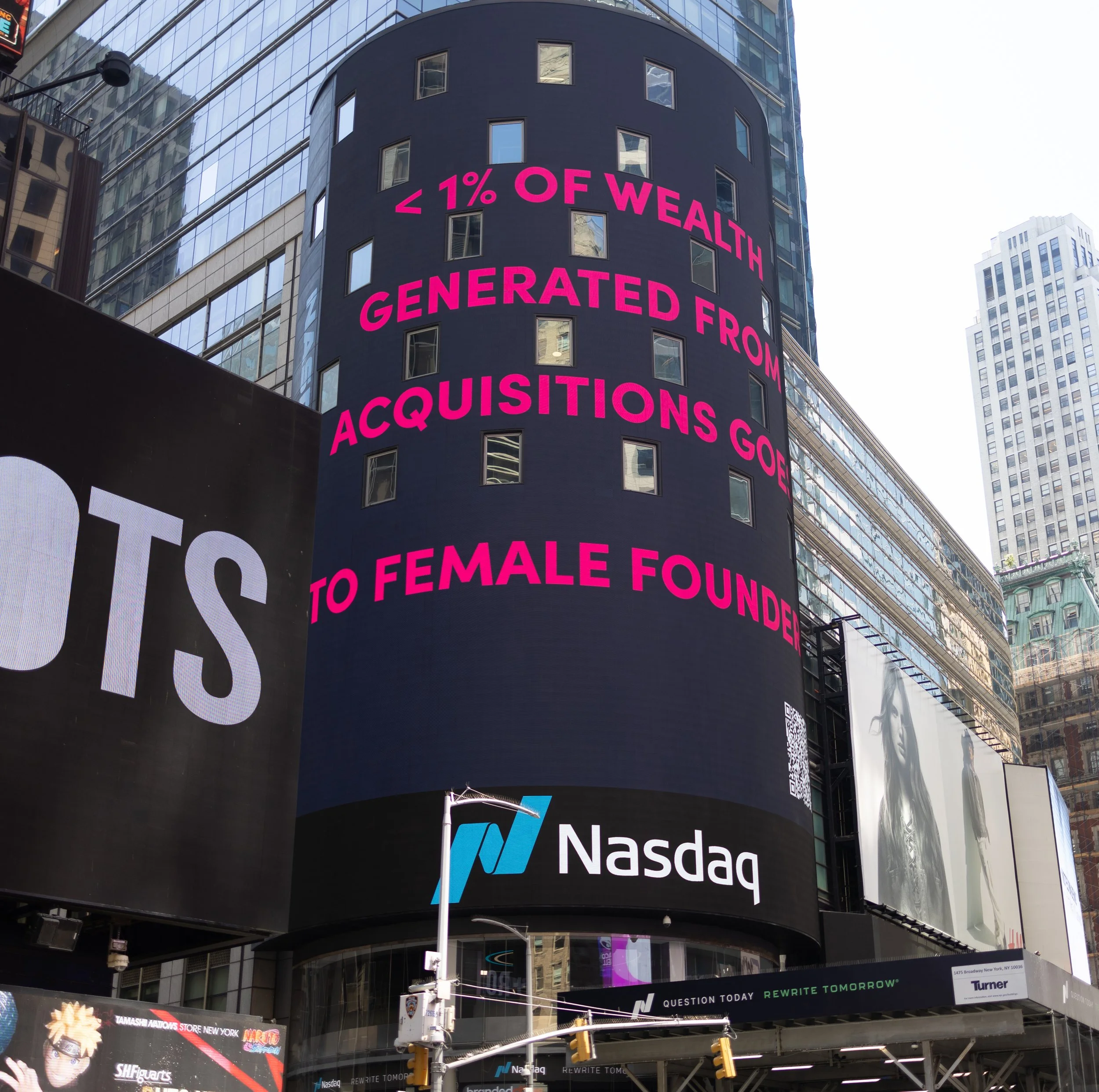 Tall building with digital billboard displaying stock market information and advertisements, with a street scene and traffic lights below.