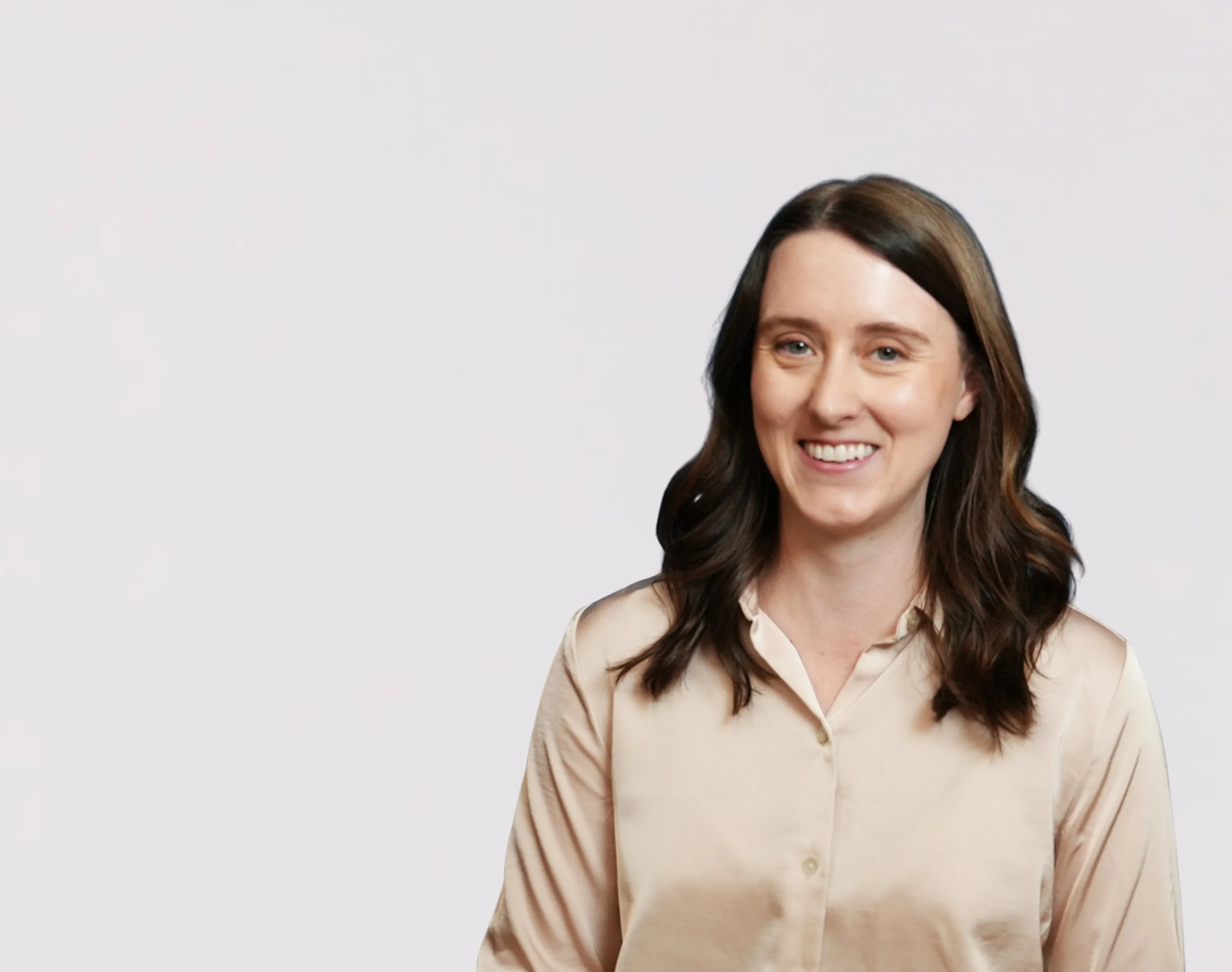 A smiling woman with long brown hair wearing a beige blouse, against a plain light background.