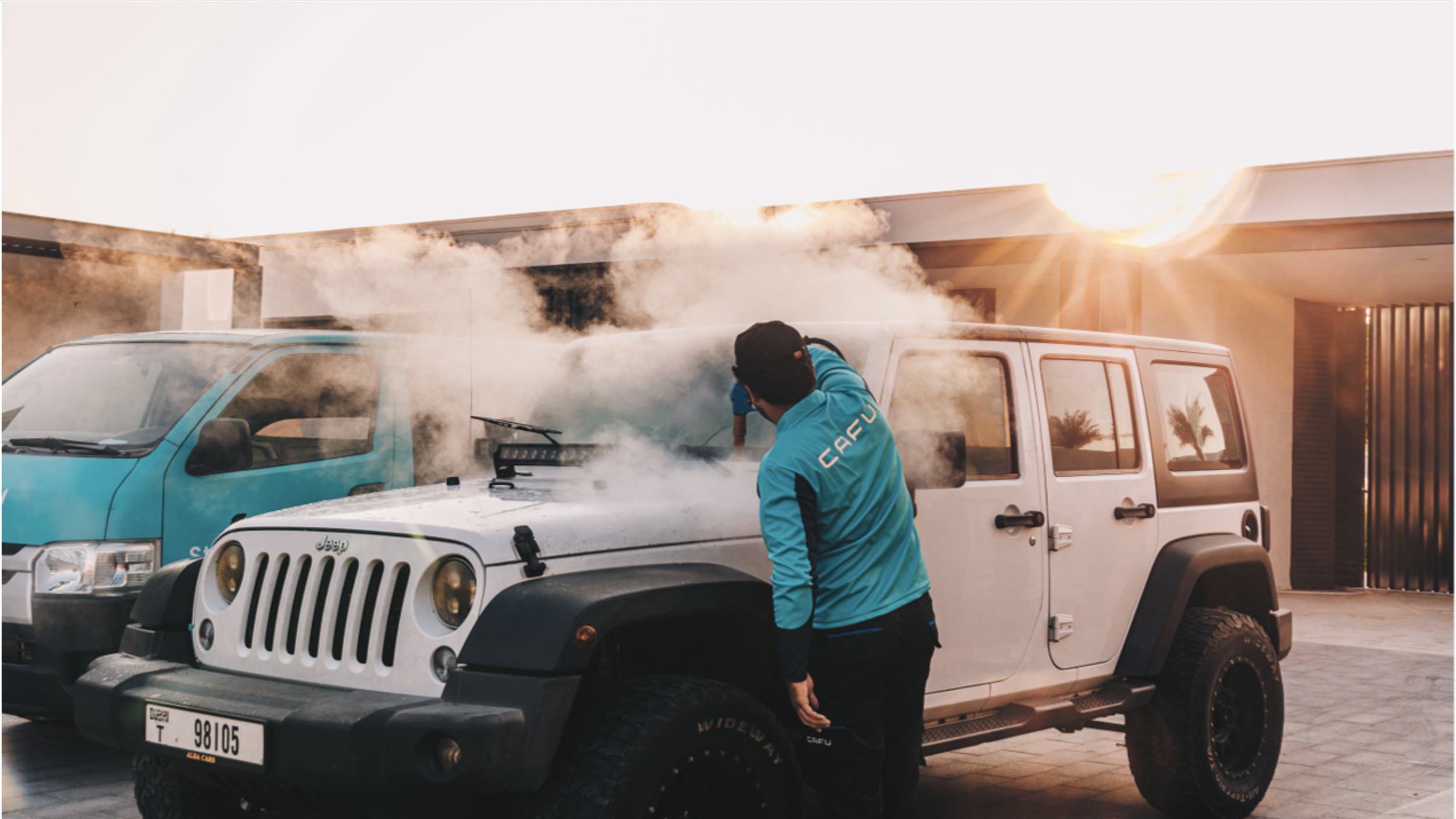 A CAFU service provider steam-cleans a white Jeep parked outside a residential building, with sunlight and steam filling the scene.