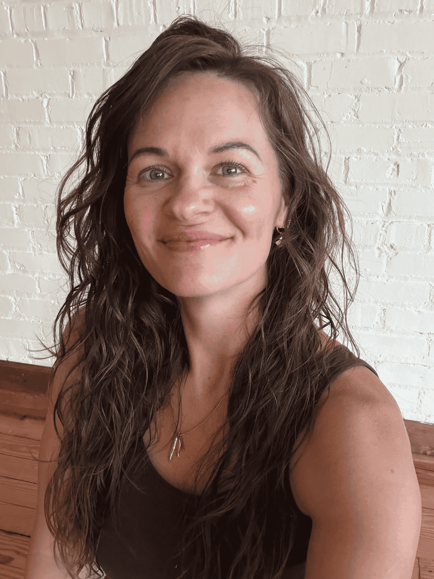 The founder, Melissa, is smiling in front of a white brick wall.