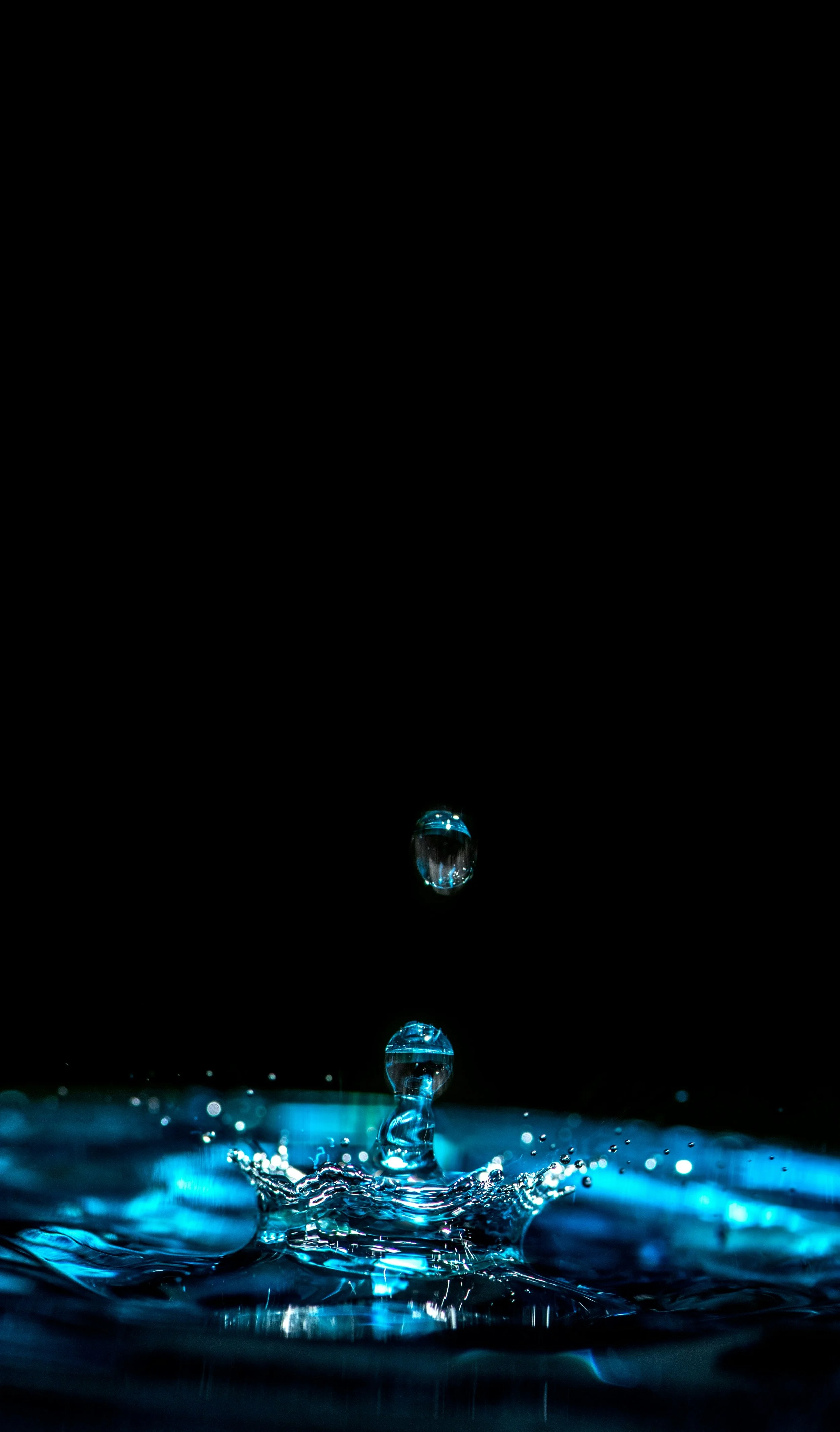 Squarespace design for entrepreneurs. Close-up of water droplets falling into water, creating a splash and ripples, with a dark background and blue lighting.