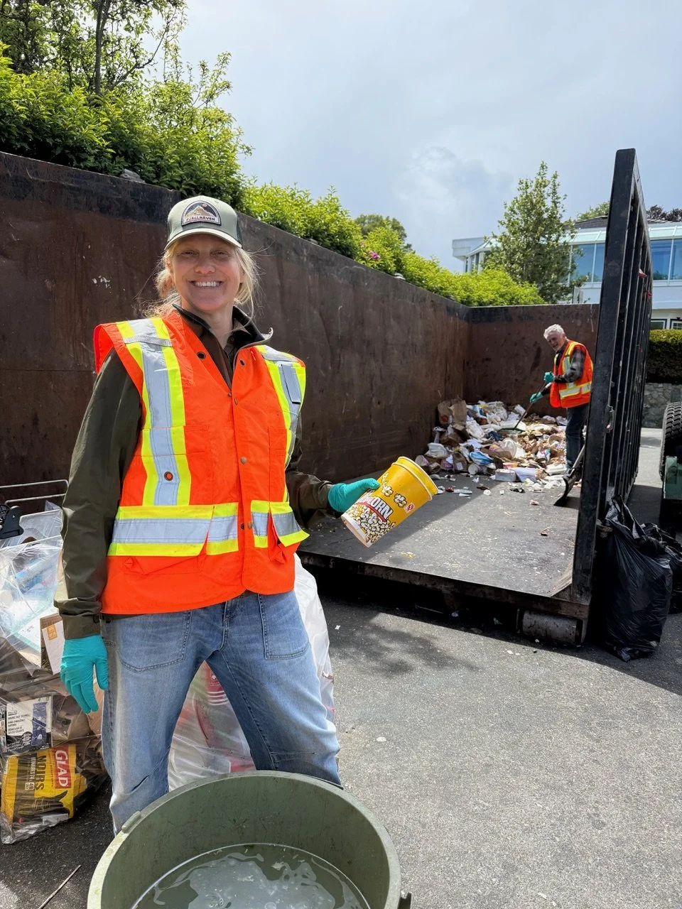 A woman smiling in a bright orange safety vest sorting waste