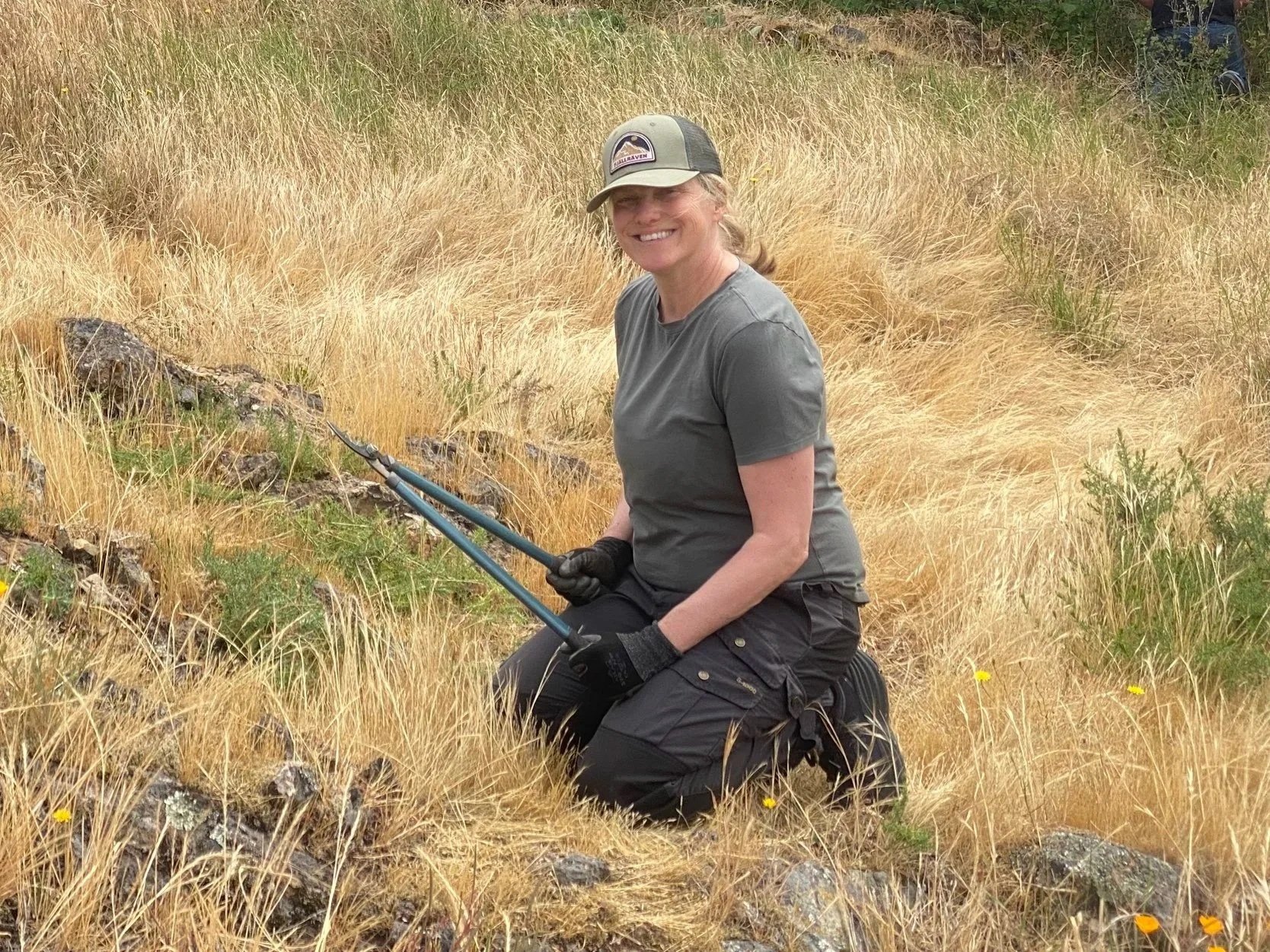 Karin Sweeney holding loppers in a yellow grass field smiling