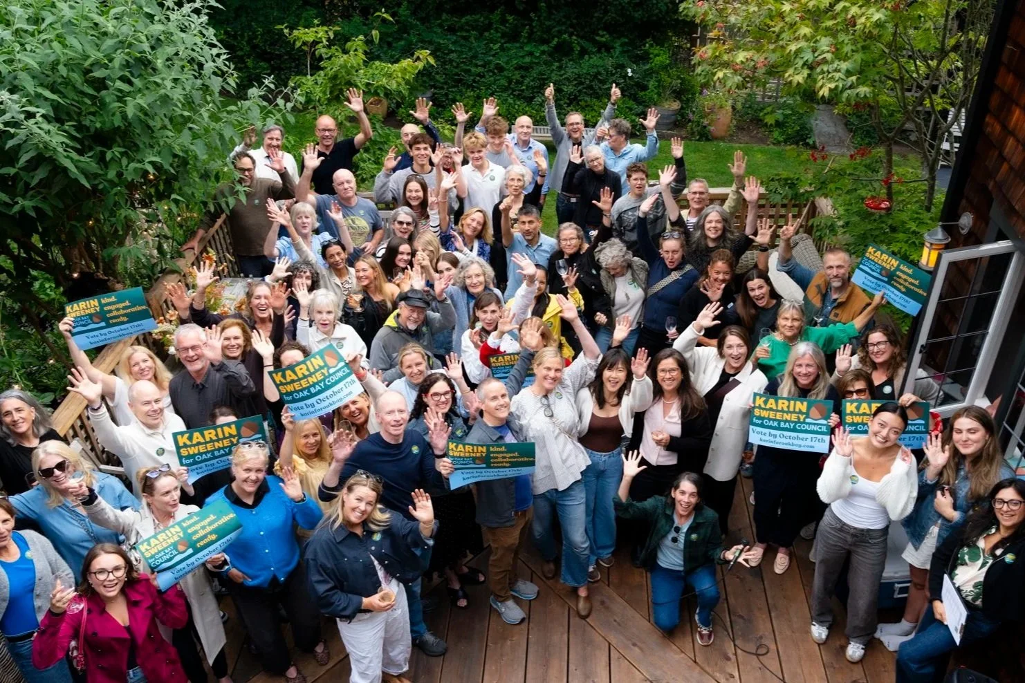 a group of people waving to the camera from a wood deck in a backyard