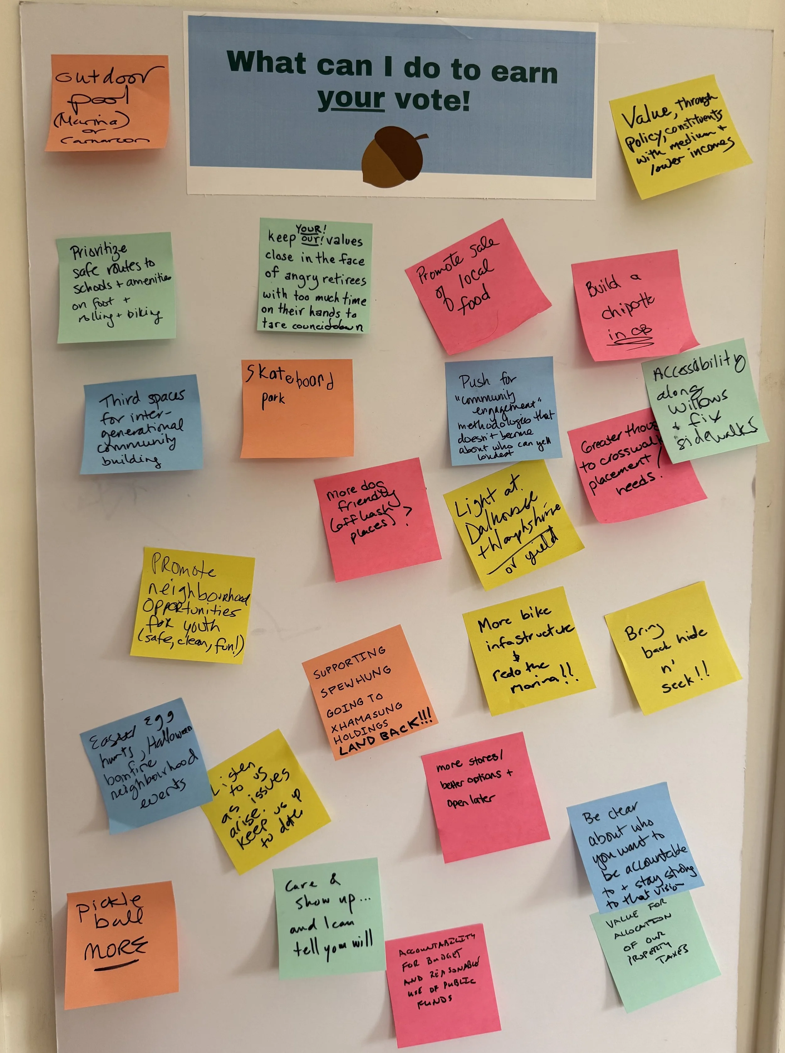 A bulletin board with multiple colorful sticky notes about community and city planning ideas. The notes include suggestions like promoting neighborhood opportunities, encouraging safe routes to school, supporting local food sales, and enhancing bicycle infrastructure.