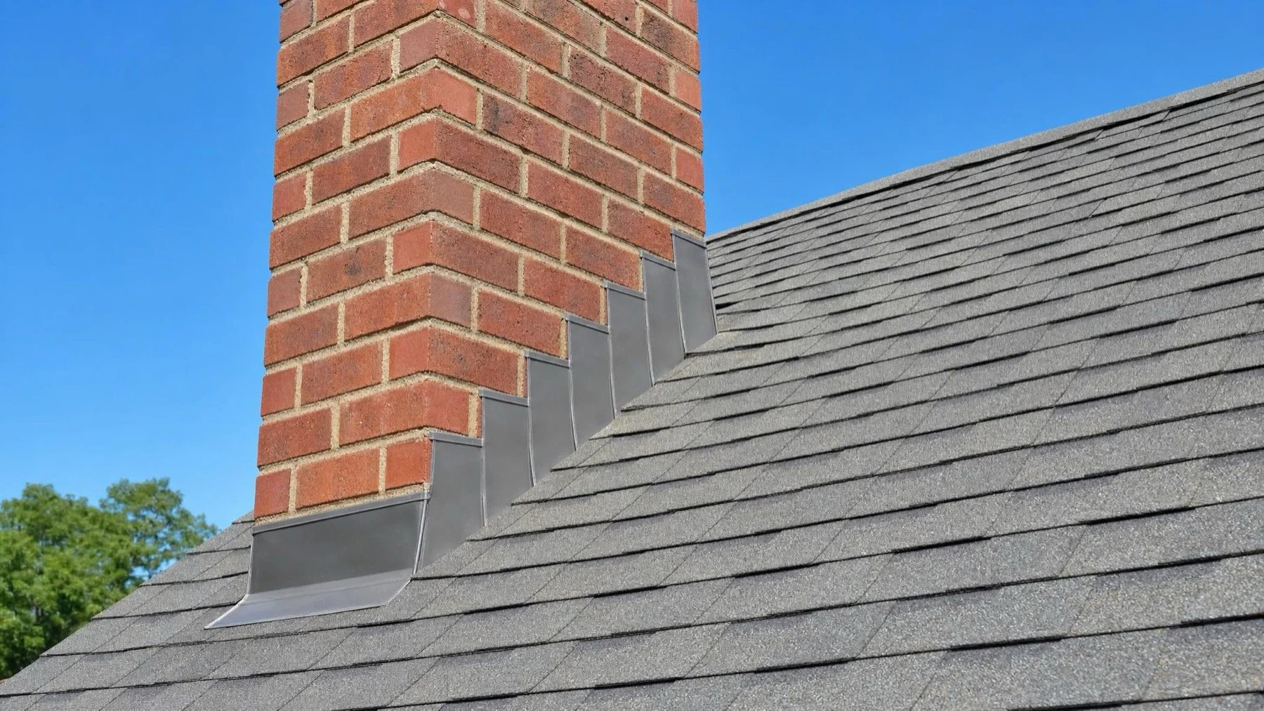 Metal step flashing where a red brick chimney meets a grey shingled roof