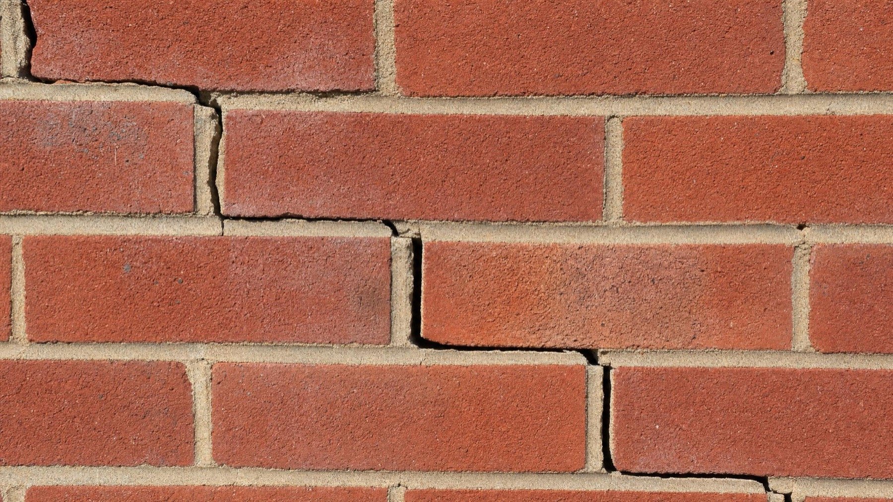 Stair-step cracks running through mortar joints in a red brick wall