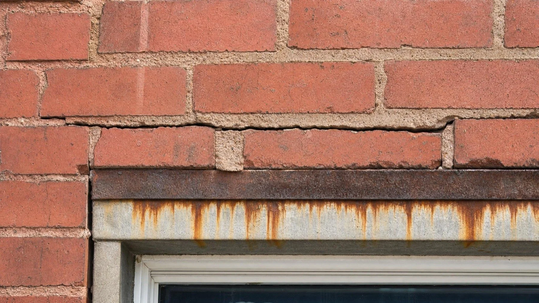 Rust staining and a cracked mortar joint above a brick window opening