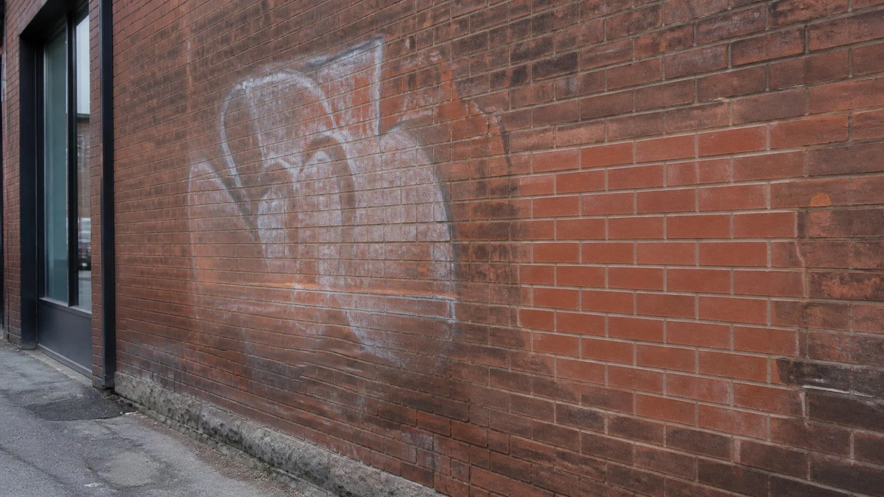 Toronto laneway brick wall with a faded graffiti mark and a clean test patch