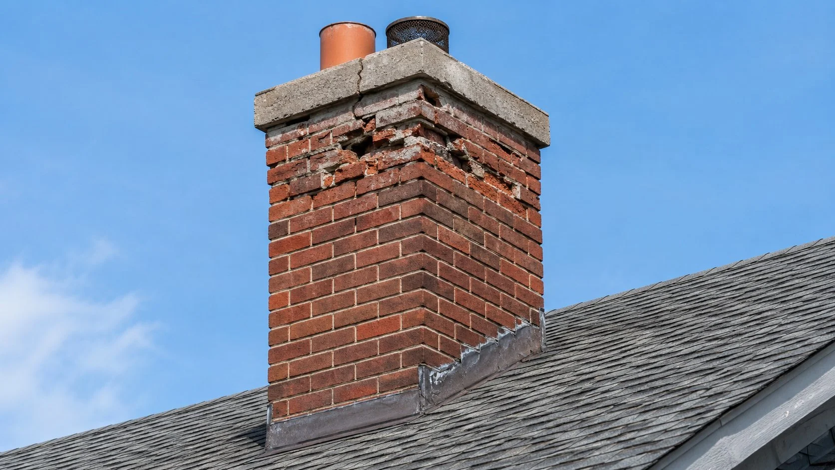 Brick chimney on a Toronto roof with a cracked crown and spalled bricks near the top