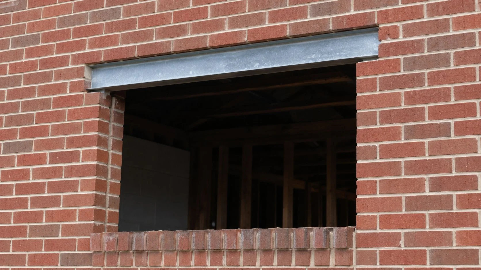 New window opening cut into an exterior brick wall with a steel lintel installed above
