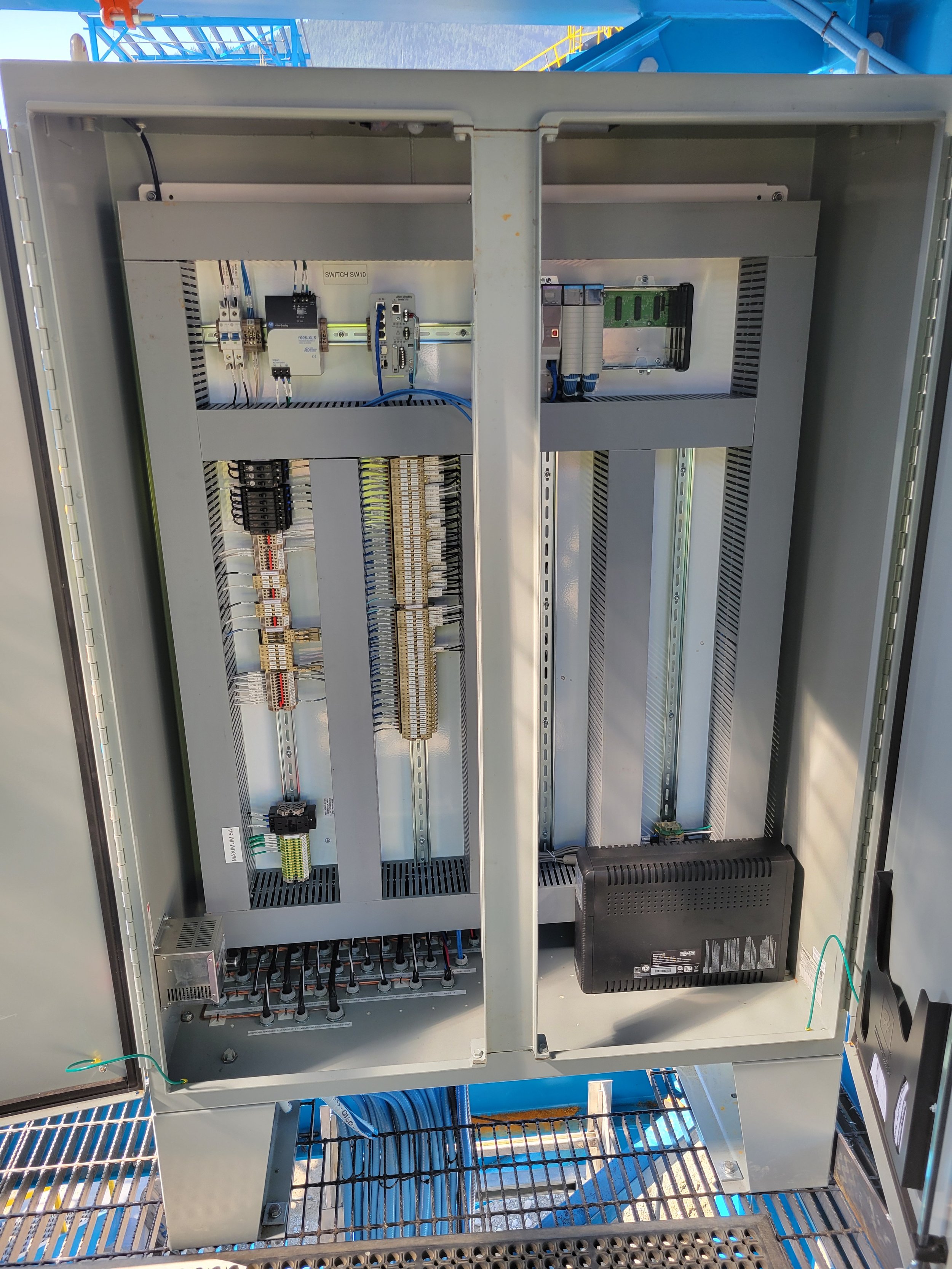 Inside an electrical control panel with various wiring, relays, and switches installed, seen from the front with the door open.