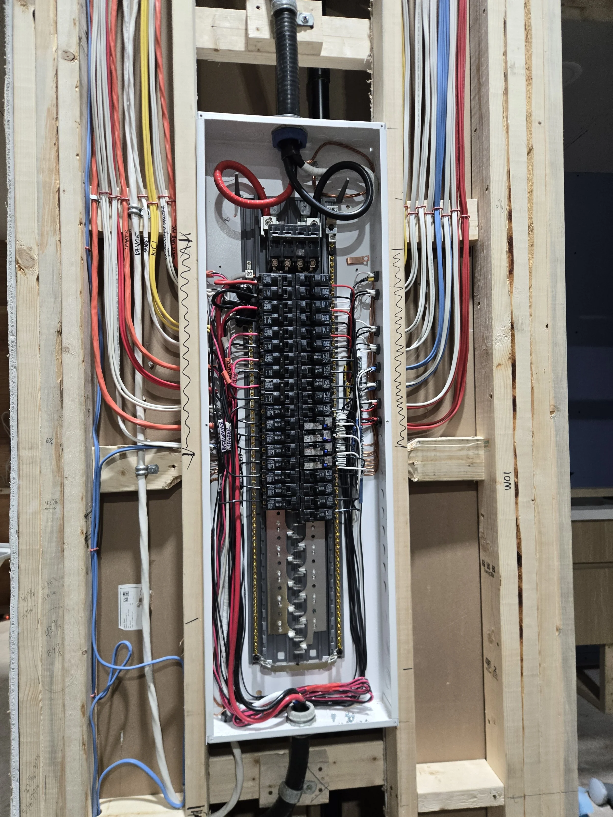 Electrical circuit breaker panel with connected wires within a wooden framing.