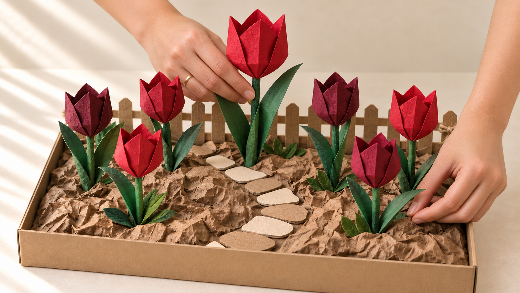 Vida’s hands arranging seven red and burgundy paper tulips at different heights in the recycled garden base.