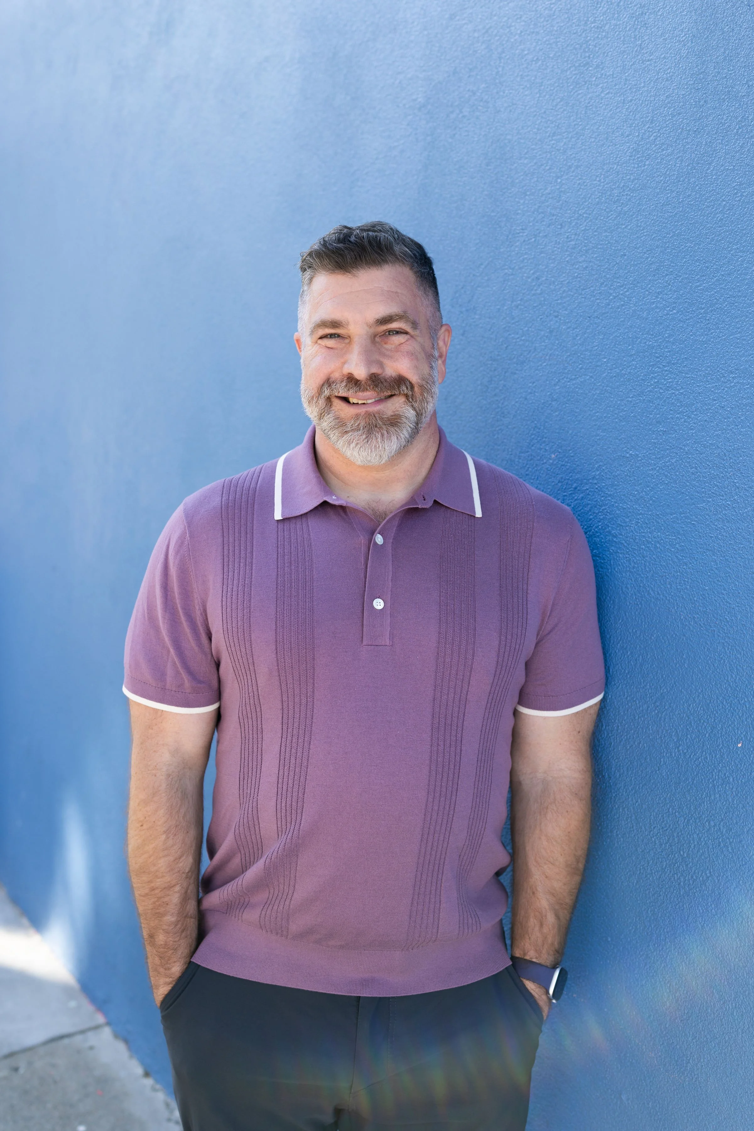 bearded man in a lavender polo against a blue wall offering therapy in San Francisco, Castro, Palm Springs, West Hollywood, and Hillcrest