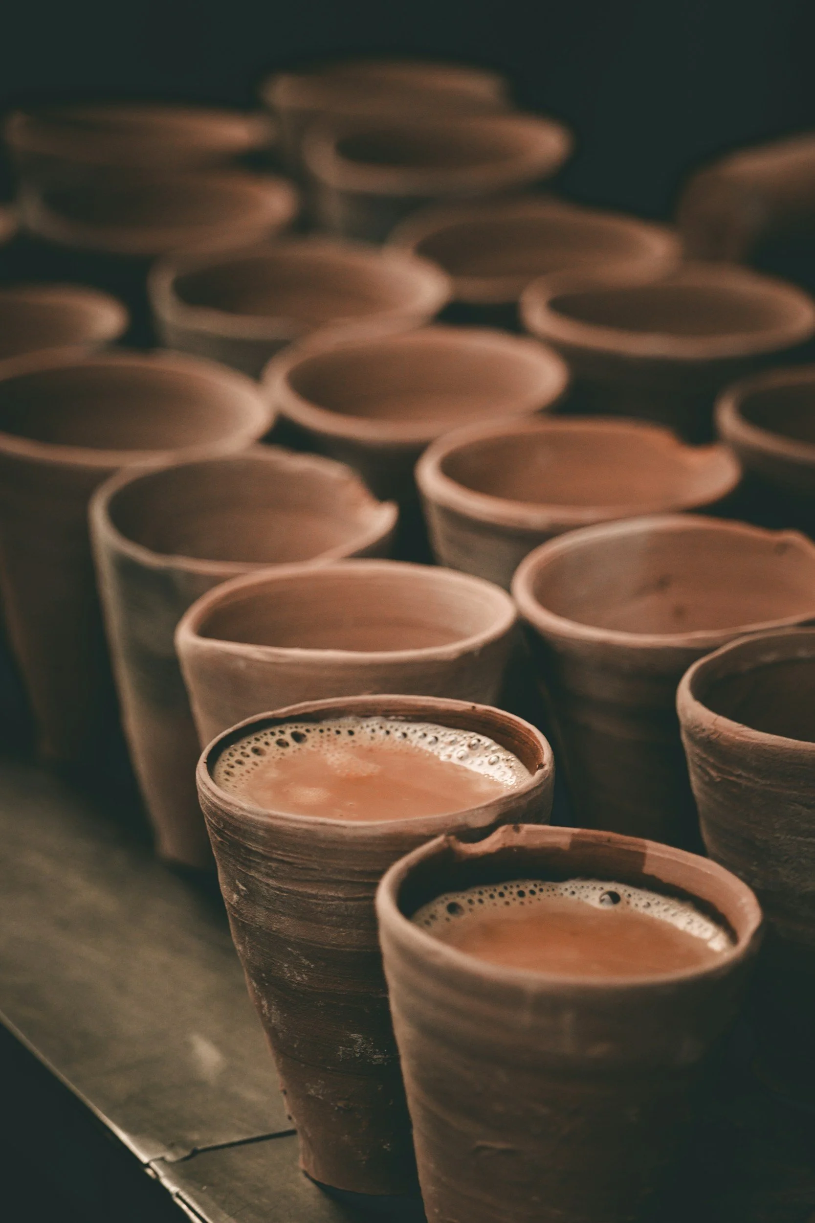 Row of ceramic cups filled with a frothy beverage, placed on a dark surface.