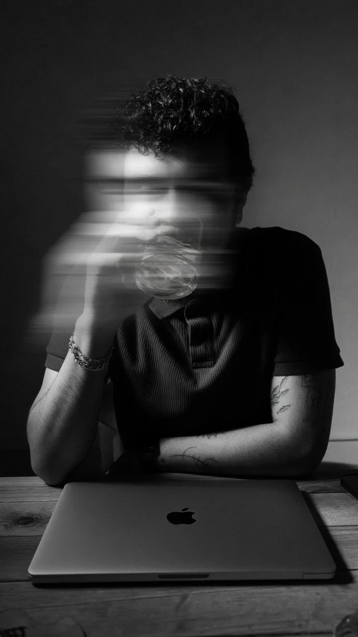 Retrato en blanco y negro de alberto sobre una mesa tomando un vaso con agua y expresión en desenfocada en movimiento