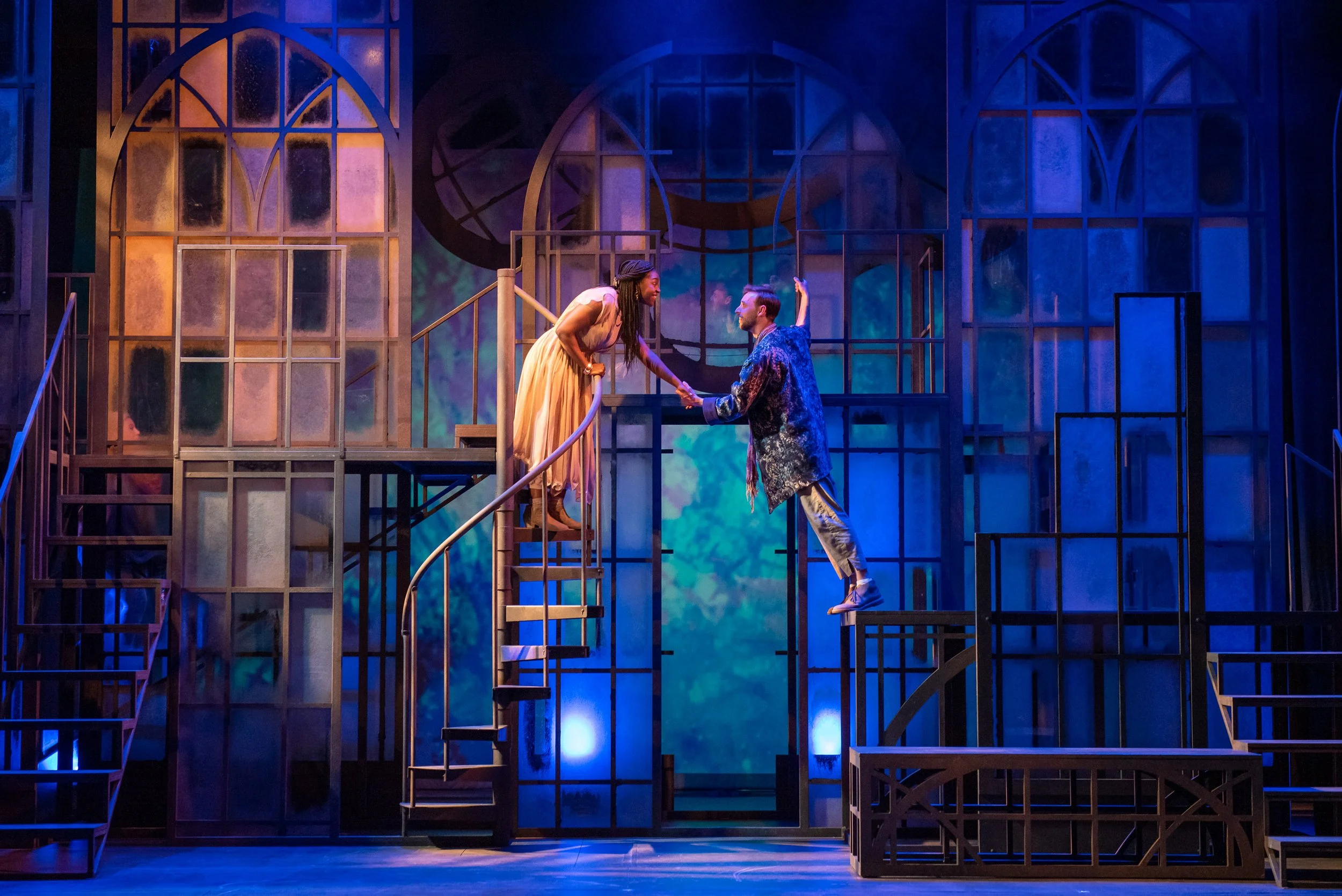 Romeo and Juliet at the Barter Theatre of Abingdon, VA.  Two actors on a theater stage facing each other, holding hands, with a multi-level geometric set in the background. The scene is lit with blue and purple lighting.