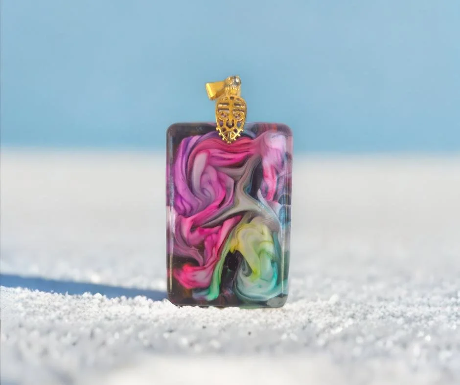 Colorful marble pendant with a gold skull charm on top, set against a bright blue sky background.