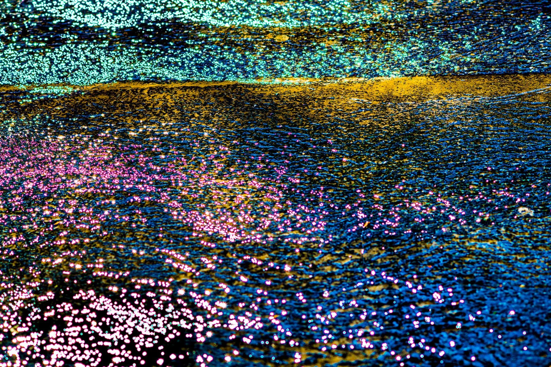 Close-up of colorful holographic glitter on a surface, reflecting light in blue, pink, yellow, and purple colors.