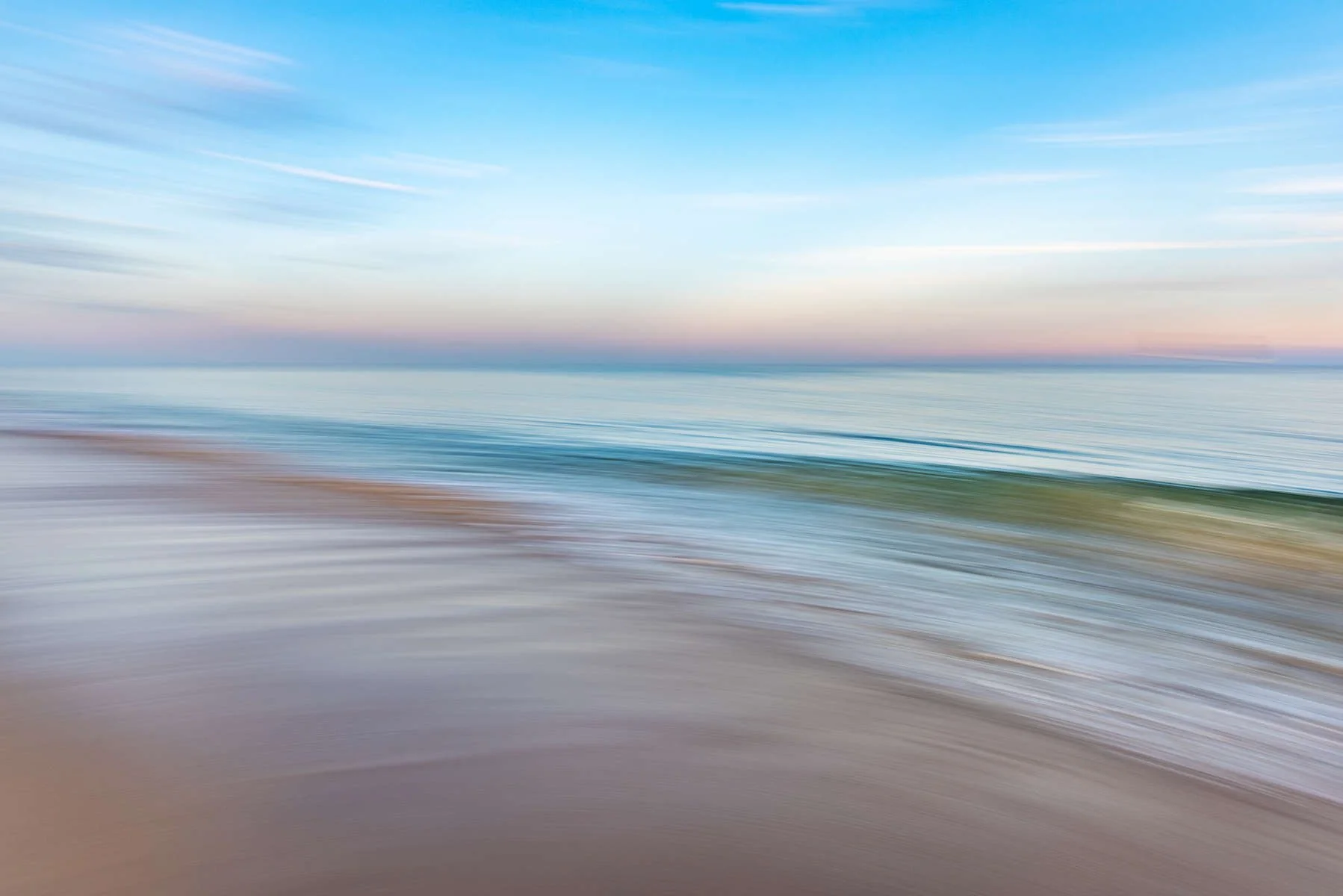 Blurry photo of a beach with ocean water, shoreline, and sky.