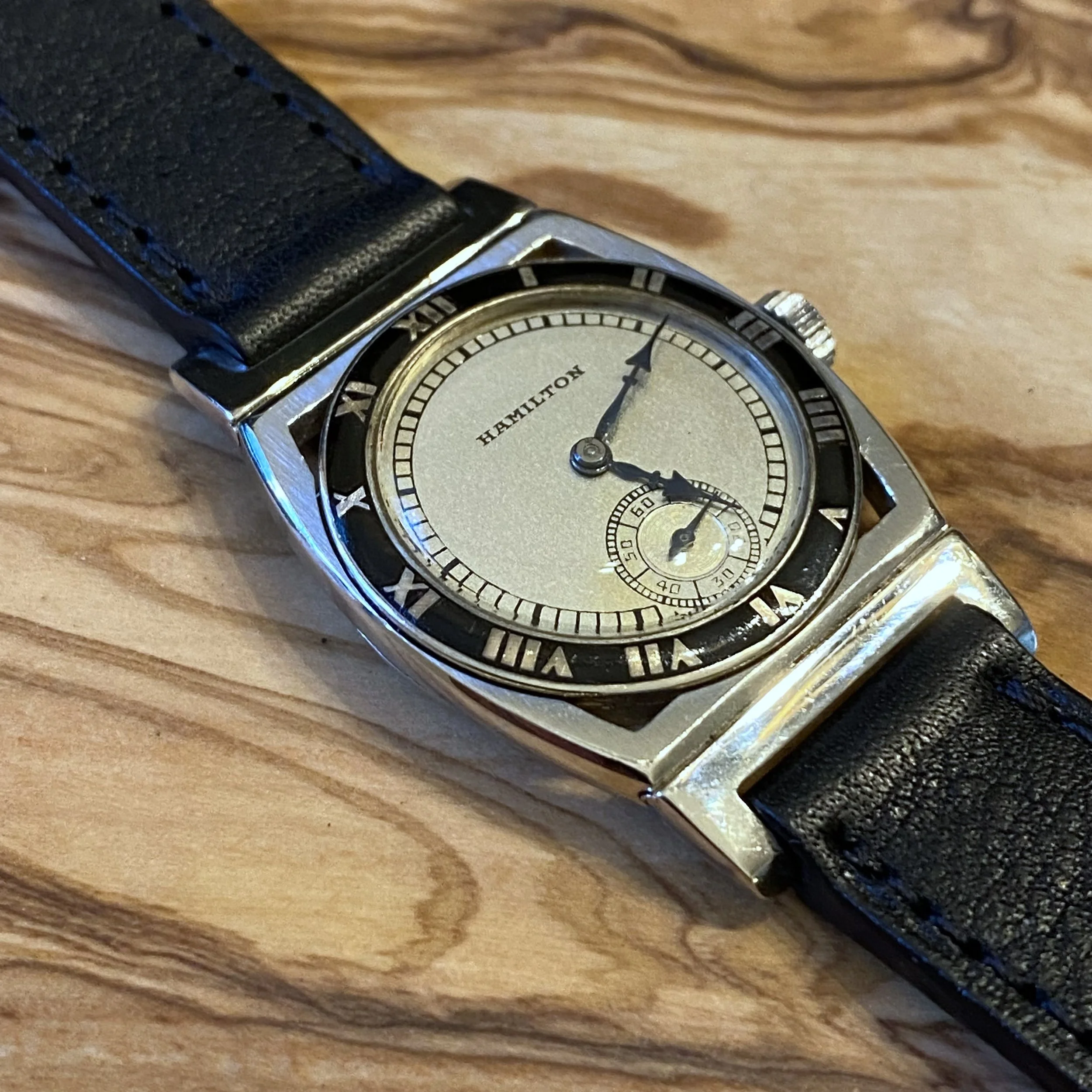 Close-up of a Hamilton wristwatch with a black strap placed on a wooden surface.