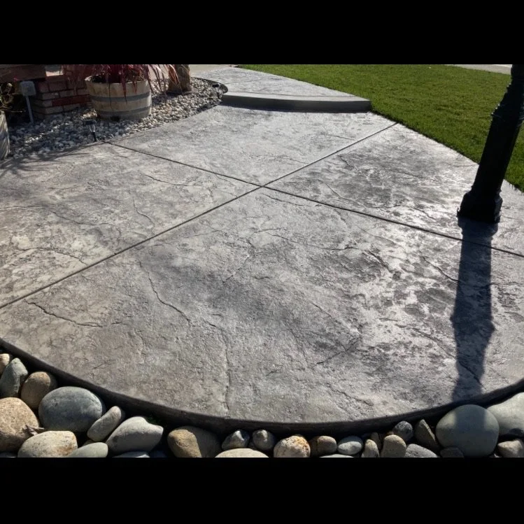 Close-up of a concrete sidewalk with visible cracks, bordered by small rocks, and a person walking on it with a green grassy area nearby.