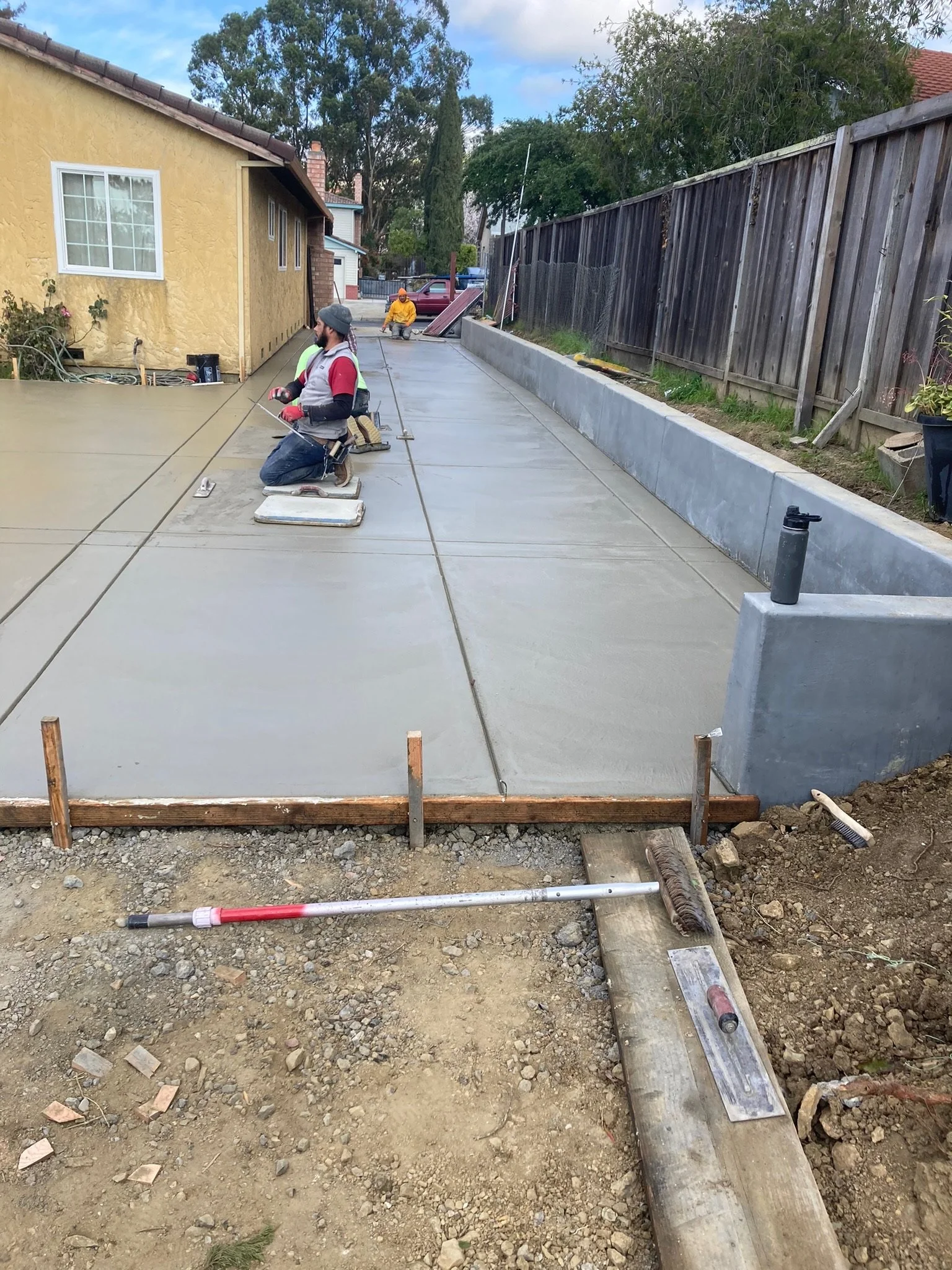 Workers constructing and finishing a concrete driveway in a residential backyard during daylight.