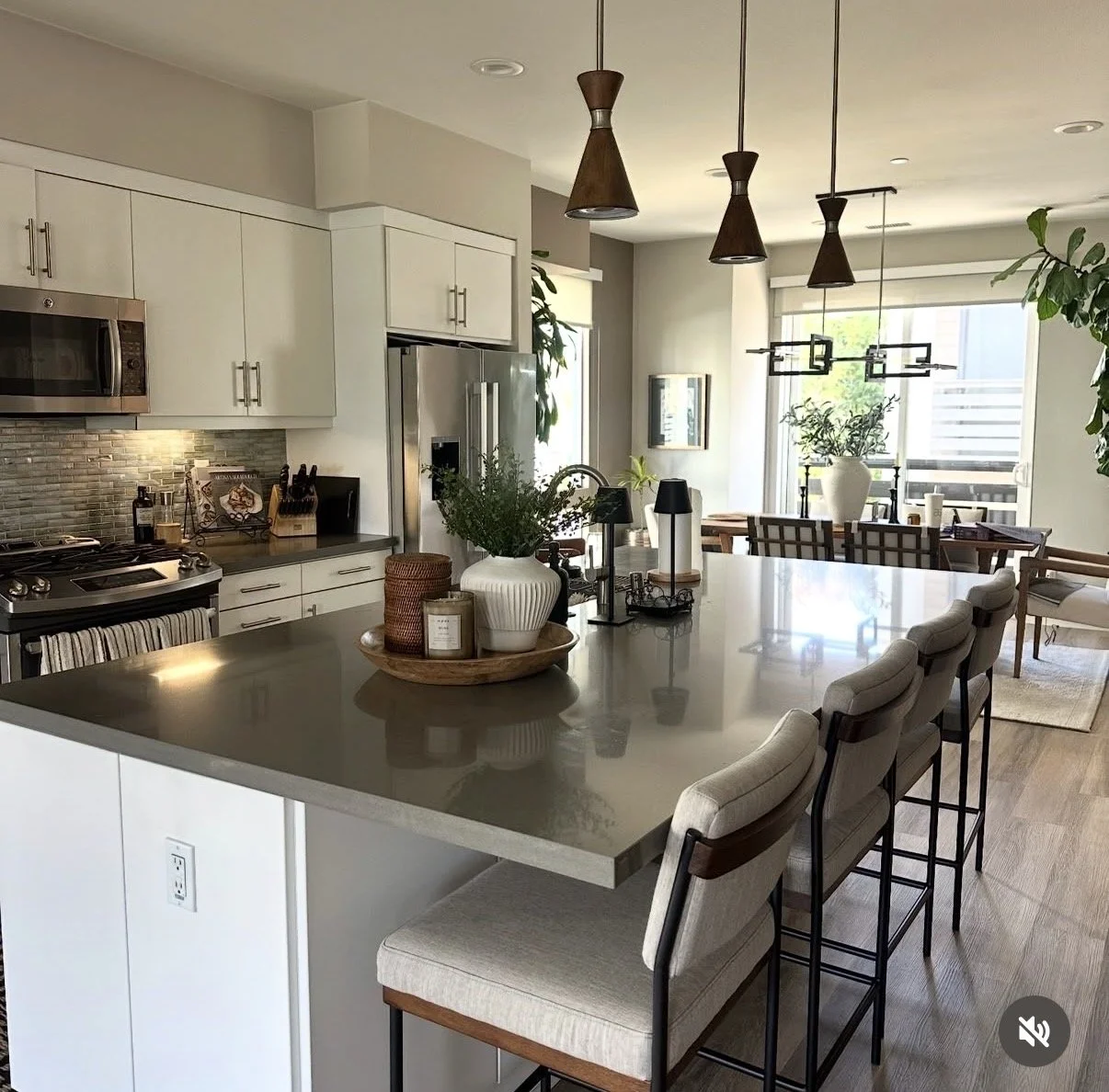 Modern kitchen and dining area with white cabinetry, stainless steel appliances, central island with barstools, pendant lighting, and large windows with outdoor views.