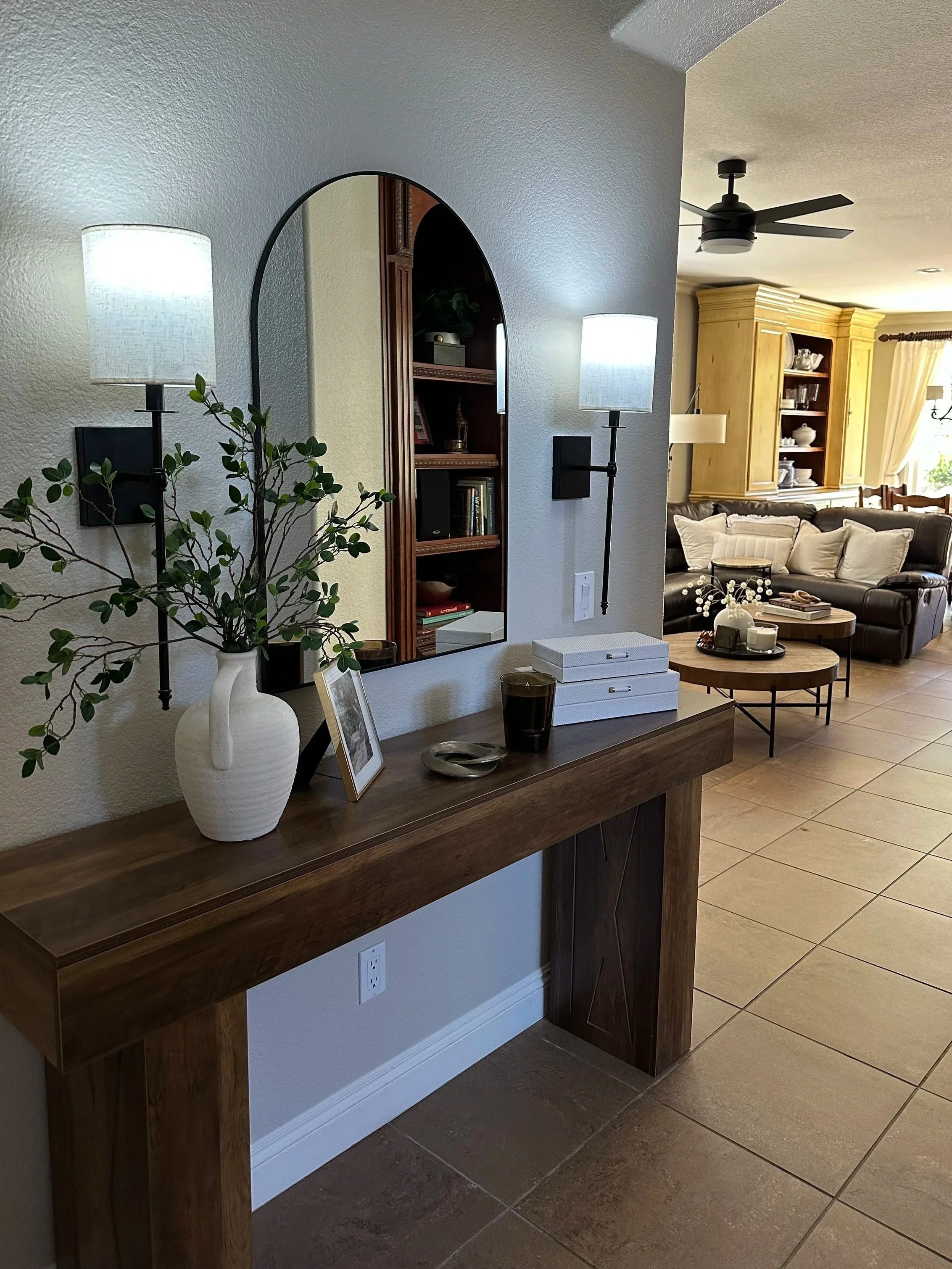 Living room with a dark leather couch, wooden cabinet, ceiling fan, and a coffee table with books and decorative items